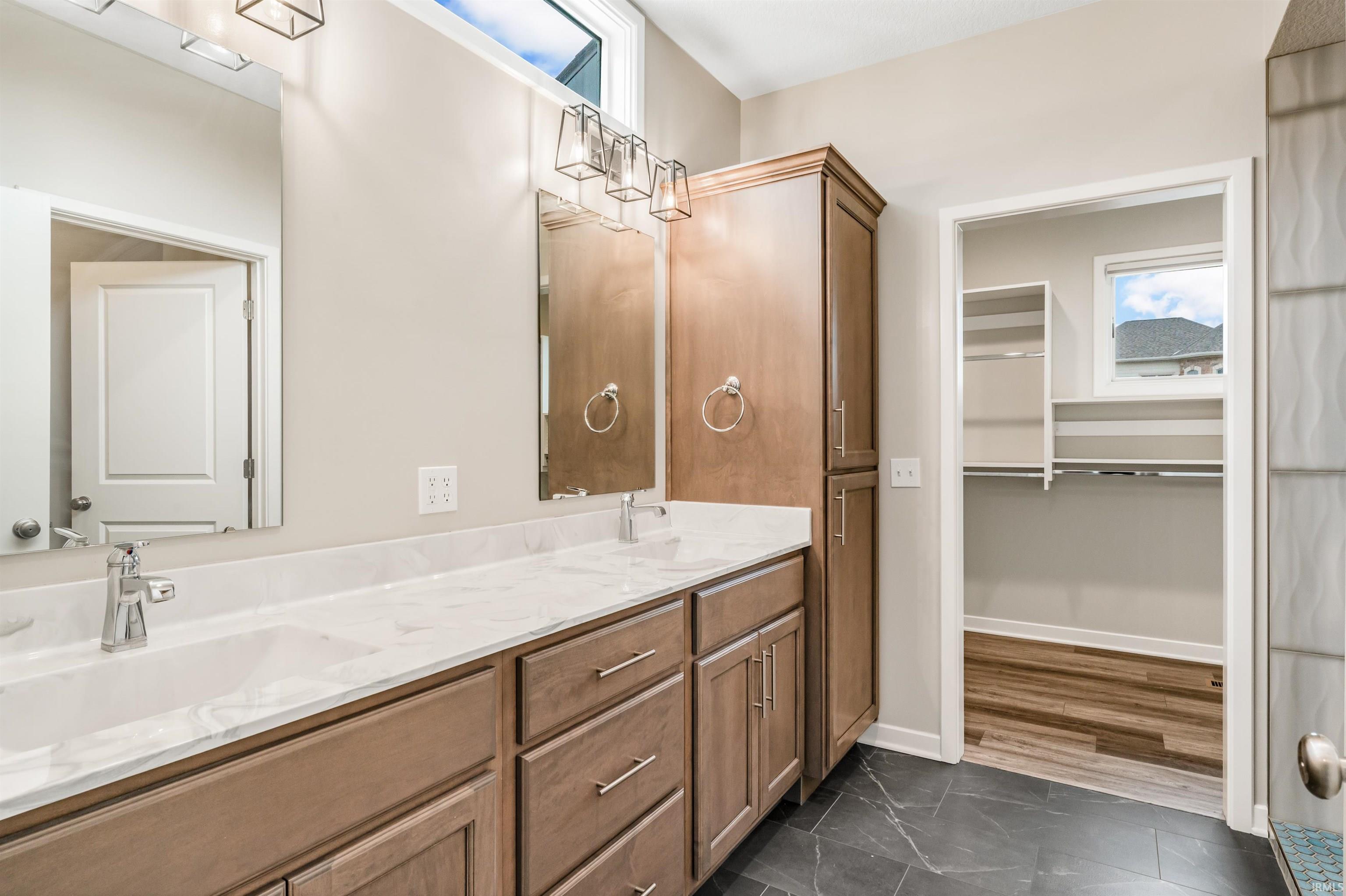 Bathroom featuring plenty of natural light, double vanity, a spacious closet, and dark marble finish floors