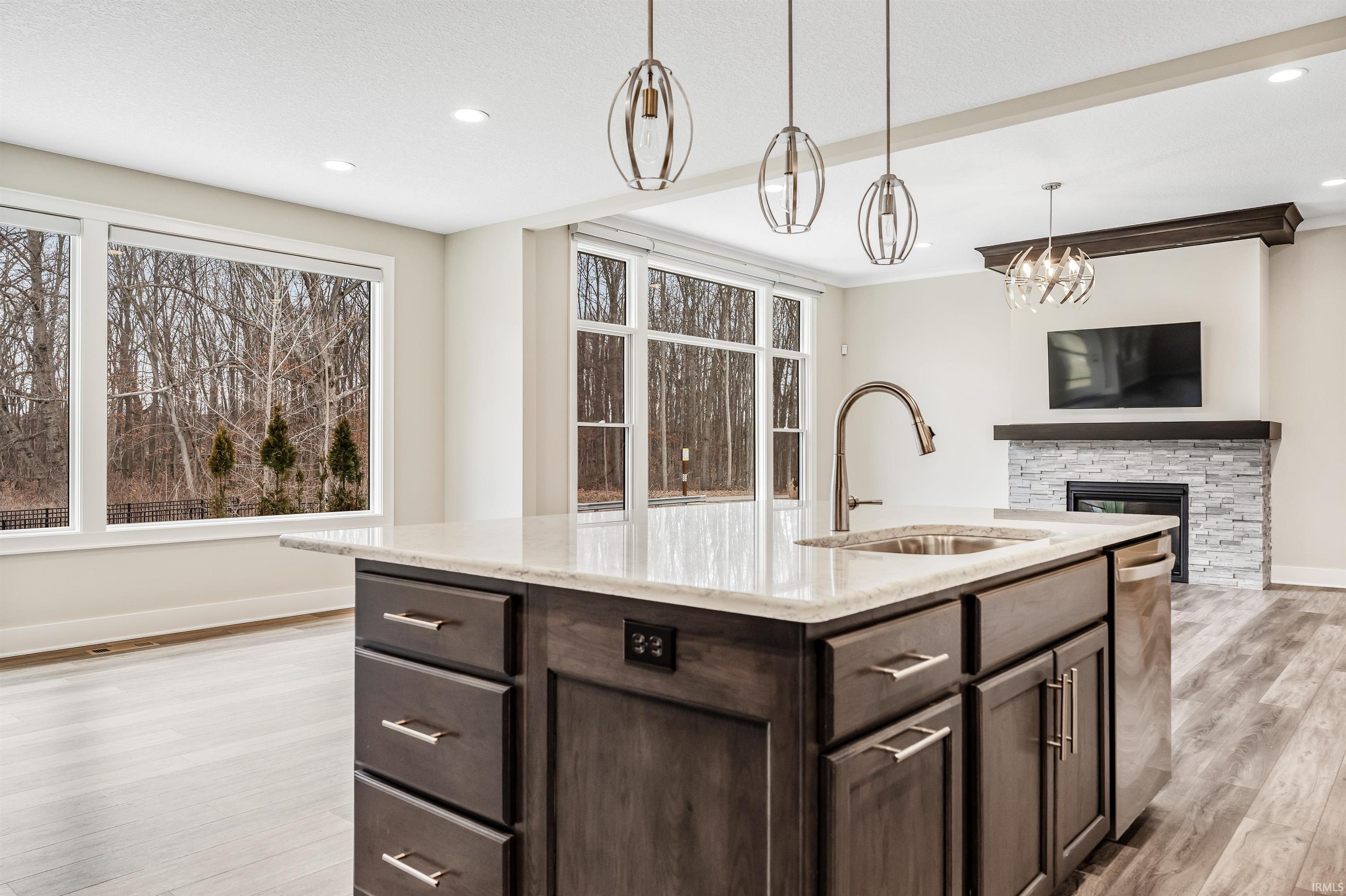 Kitchen featuring dark wood finish cabinetry, light wood-type flooring, a fireplace, open floor plan, and a kitchen island with sink