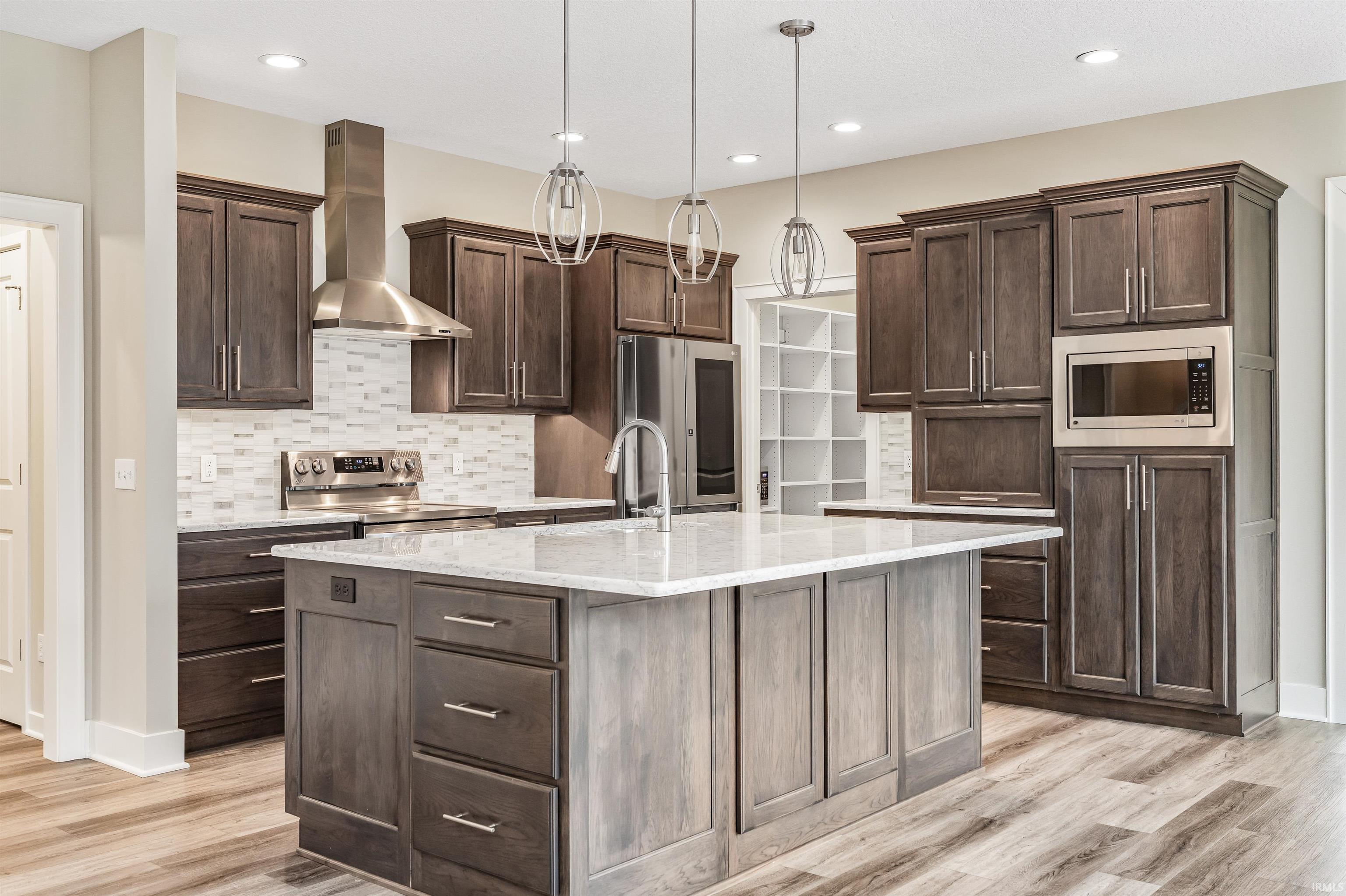 Kitchen with dark wood finish cabinets, hanging light fixtures, light stone countertops, stainless steel appliances, and tasteful backsplash