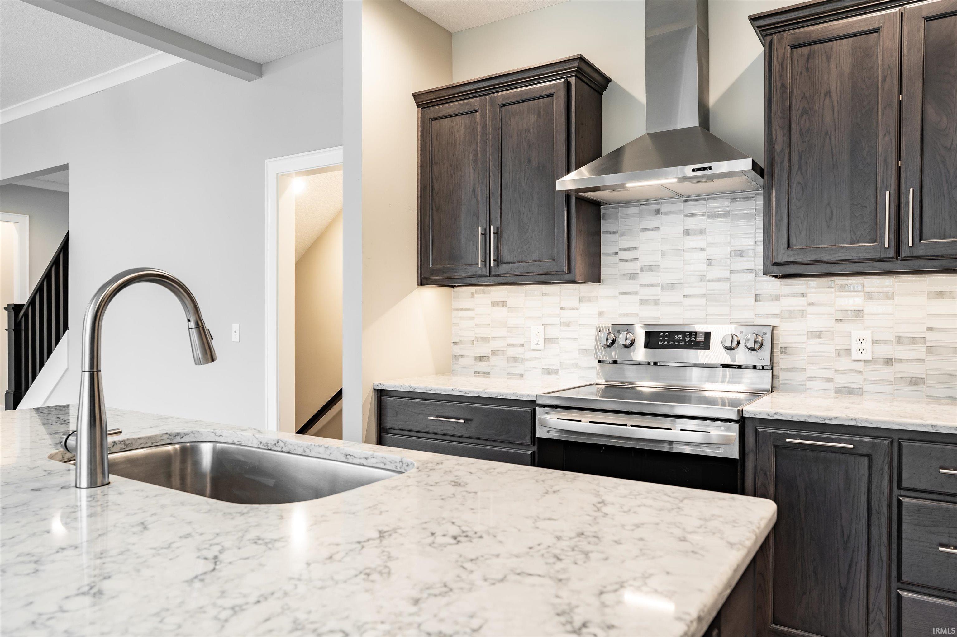 Kitchen with stainless steel electric range, light stone countertops, dark wood finish cabinets, beam ceiling, and decorative backsplash