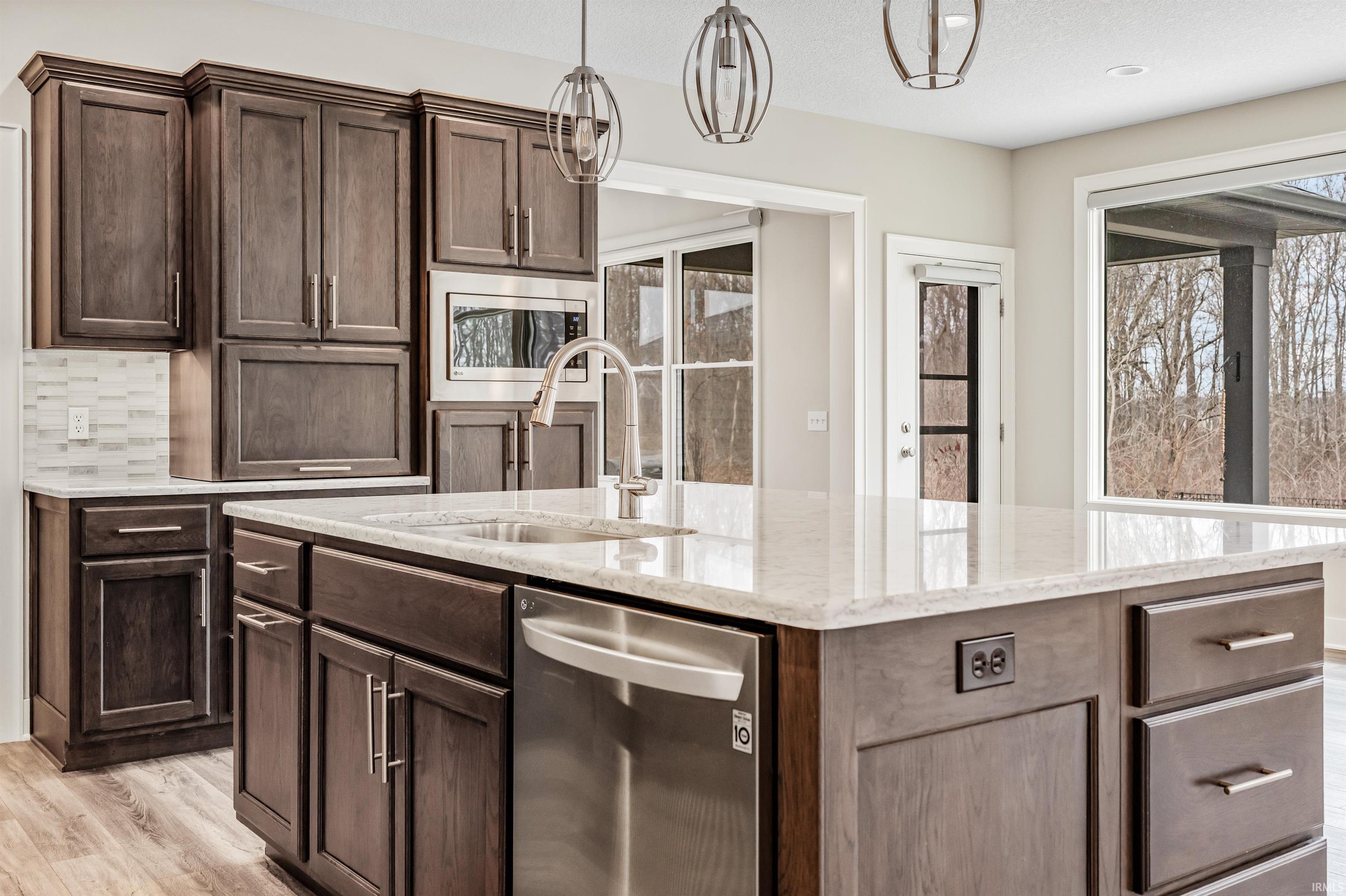 Kitchen with stainless steel appliances, light stone countertops, dark wood finish cabinets, light wood-type flooring, and decorative light fixtures