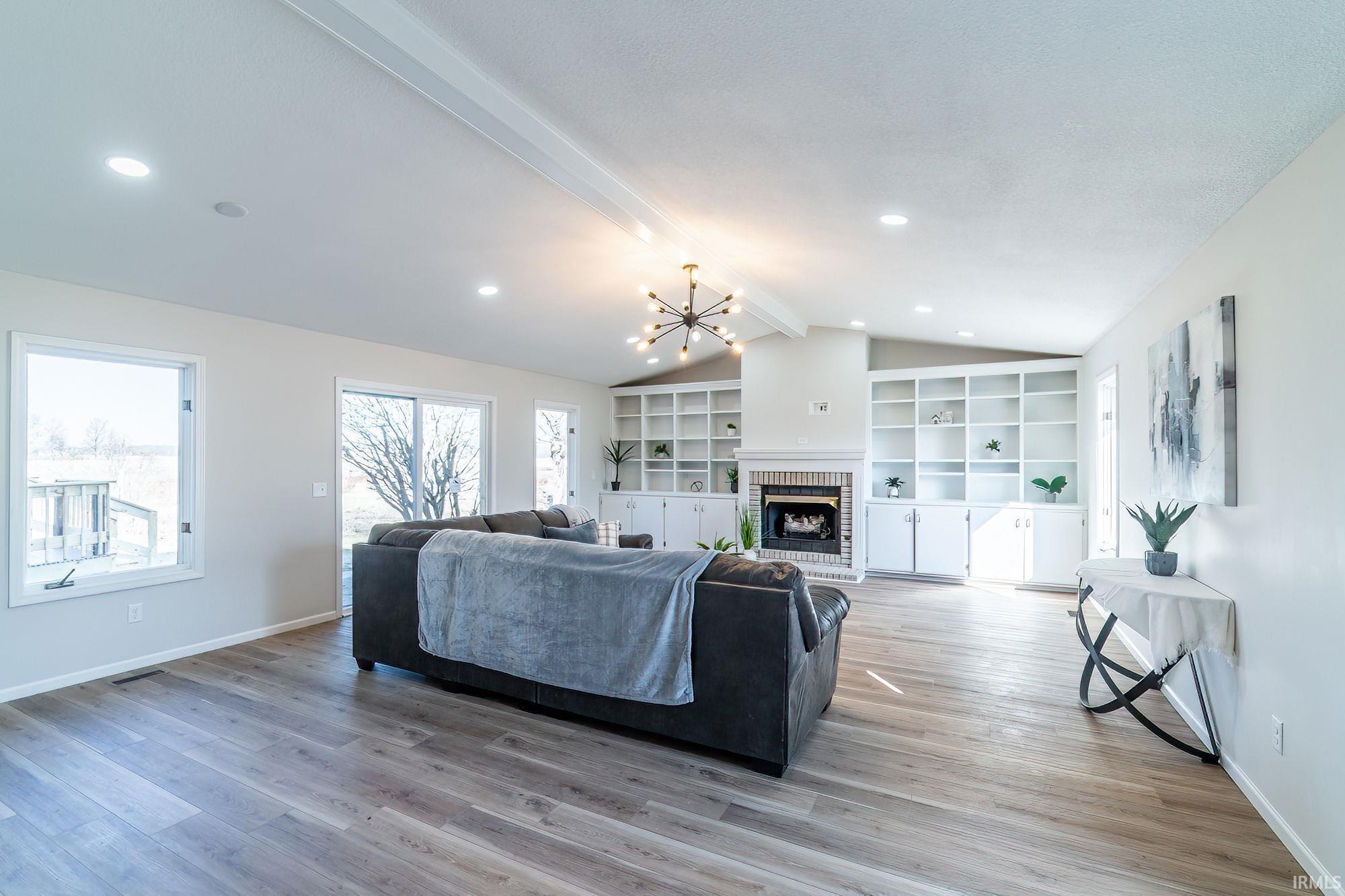 Living area with hanging lights, beamed ceiling, light wood-style floors, a brick fireplace, and built in shelves