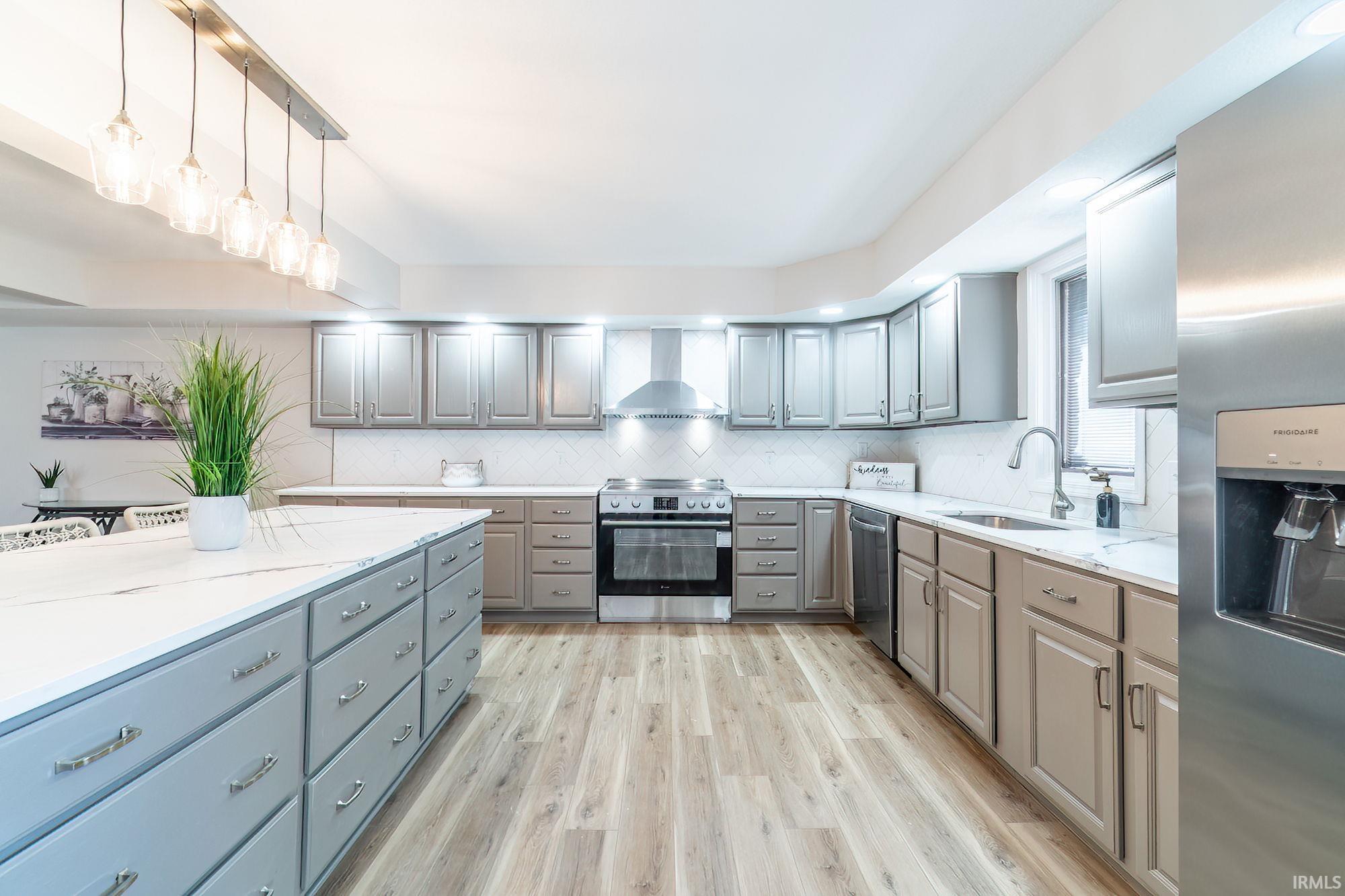 Kitchen featuring stainless steel appliances, gray cabinets, light stone counters, and light wood-style floors