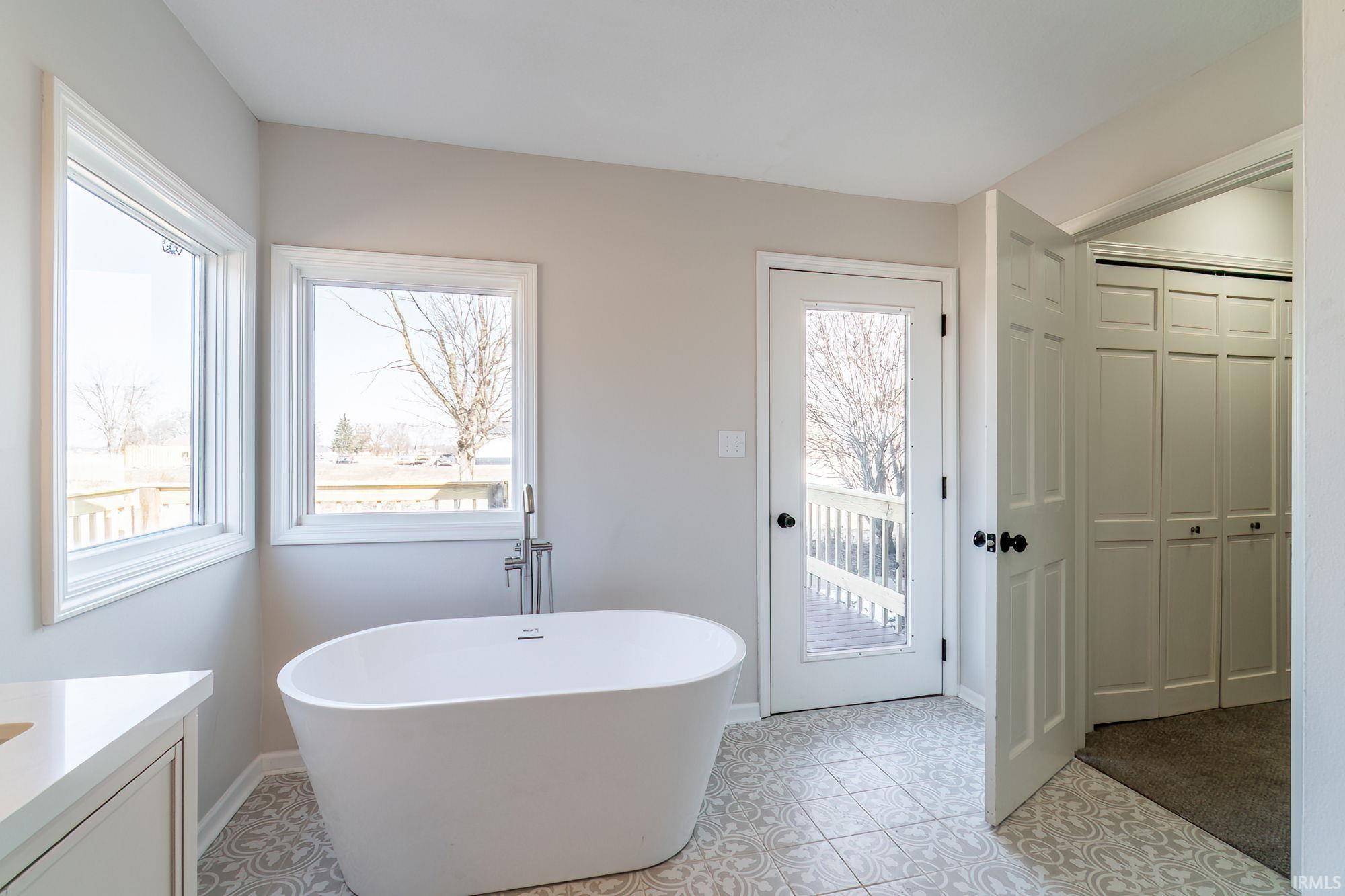Full bath featuring vanity, a closet, a soaking tub, and light tile patterned flooring