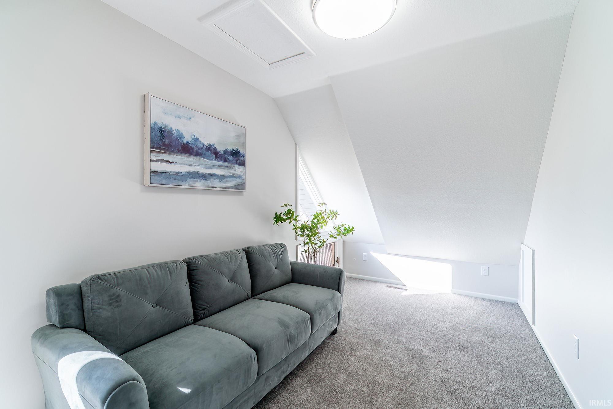 Carpeted living room with attic access and lofted ceiling