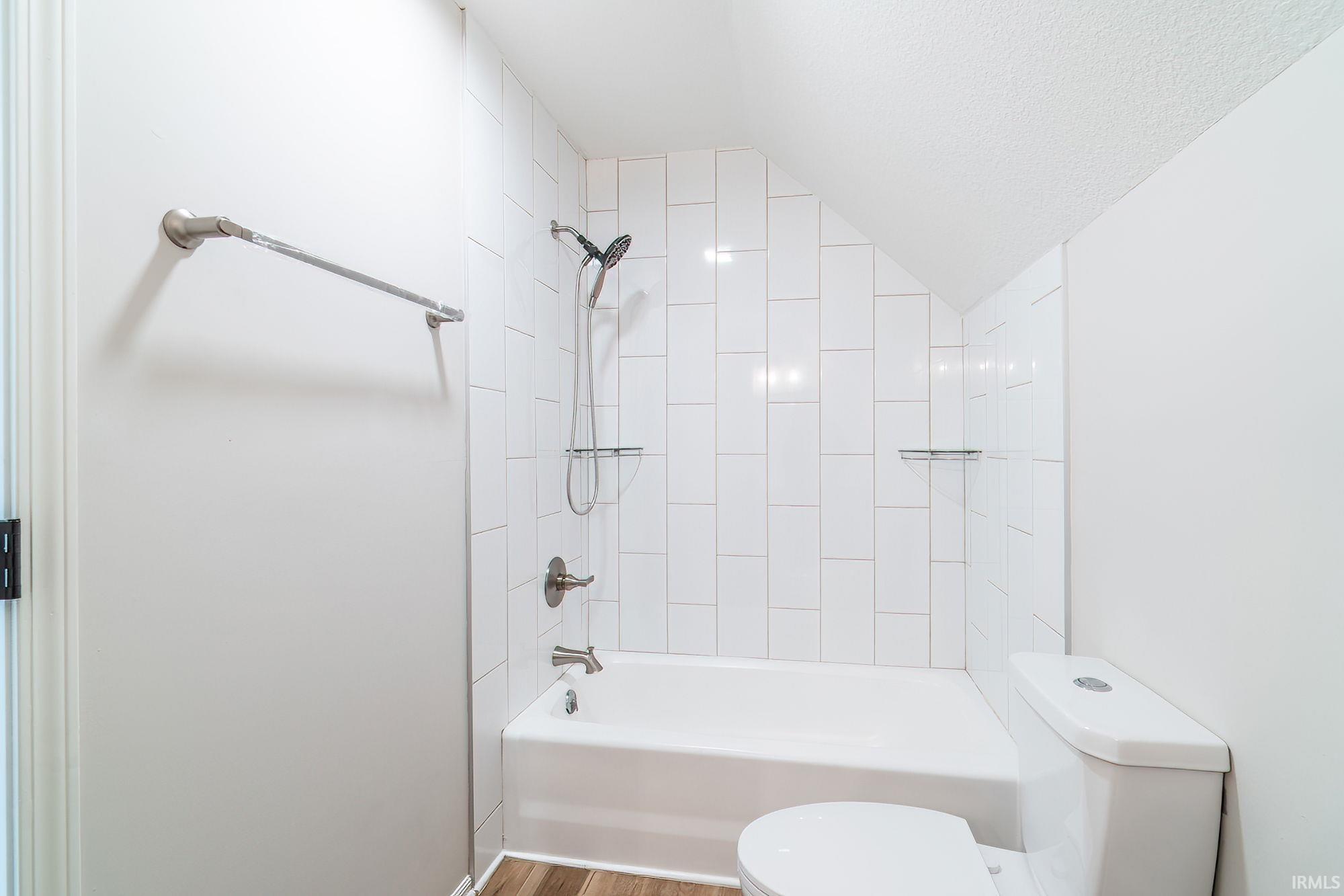 Full bath featuring shower / washtub combination, vaulted ceiling, and wood finished floors