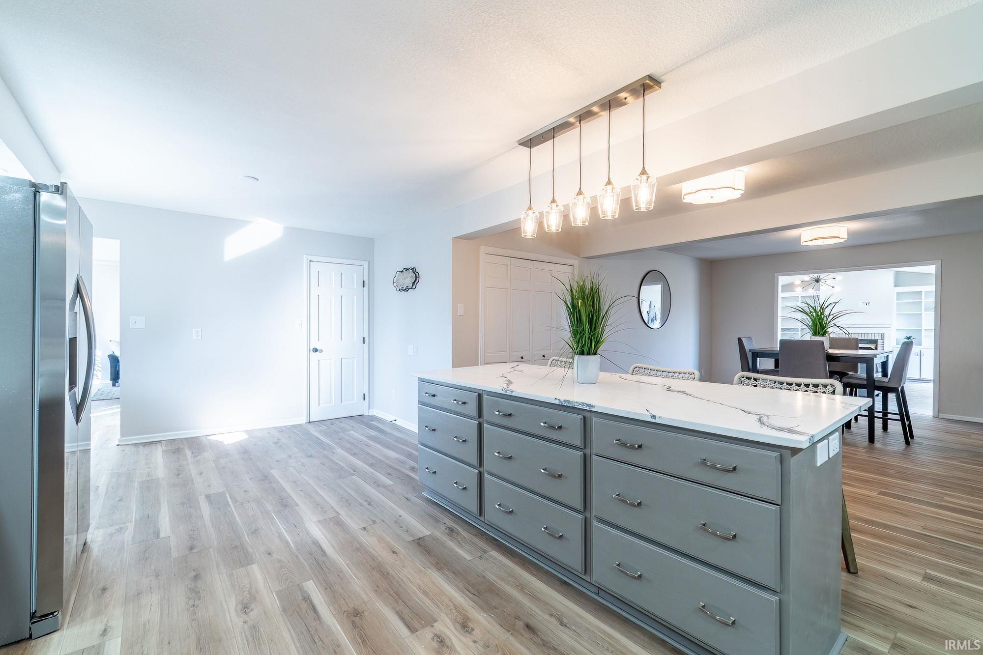 Kitchen featuring a center island, stainless steel refrigerator with ice dispenser, light stone countertops, pendant lighting, and light wood-type flooring