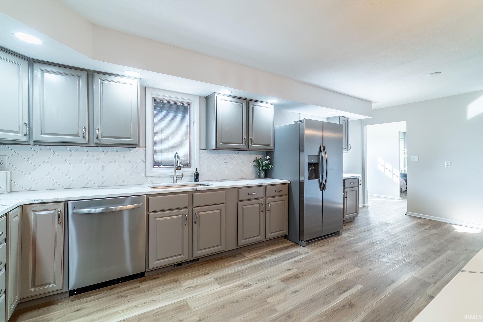 Kitchen featuring gray cabinetry, stainless steel appliances, backsplash, light wood finished floors, and light stone countertops
