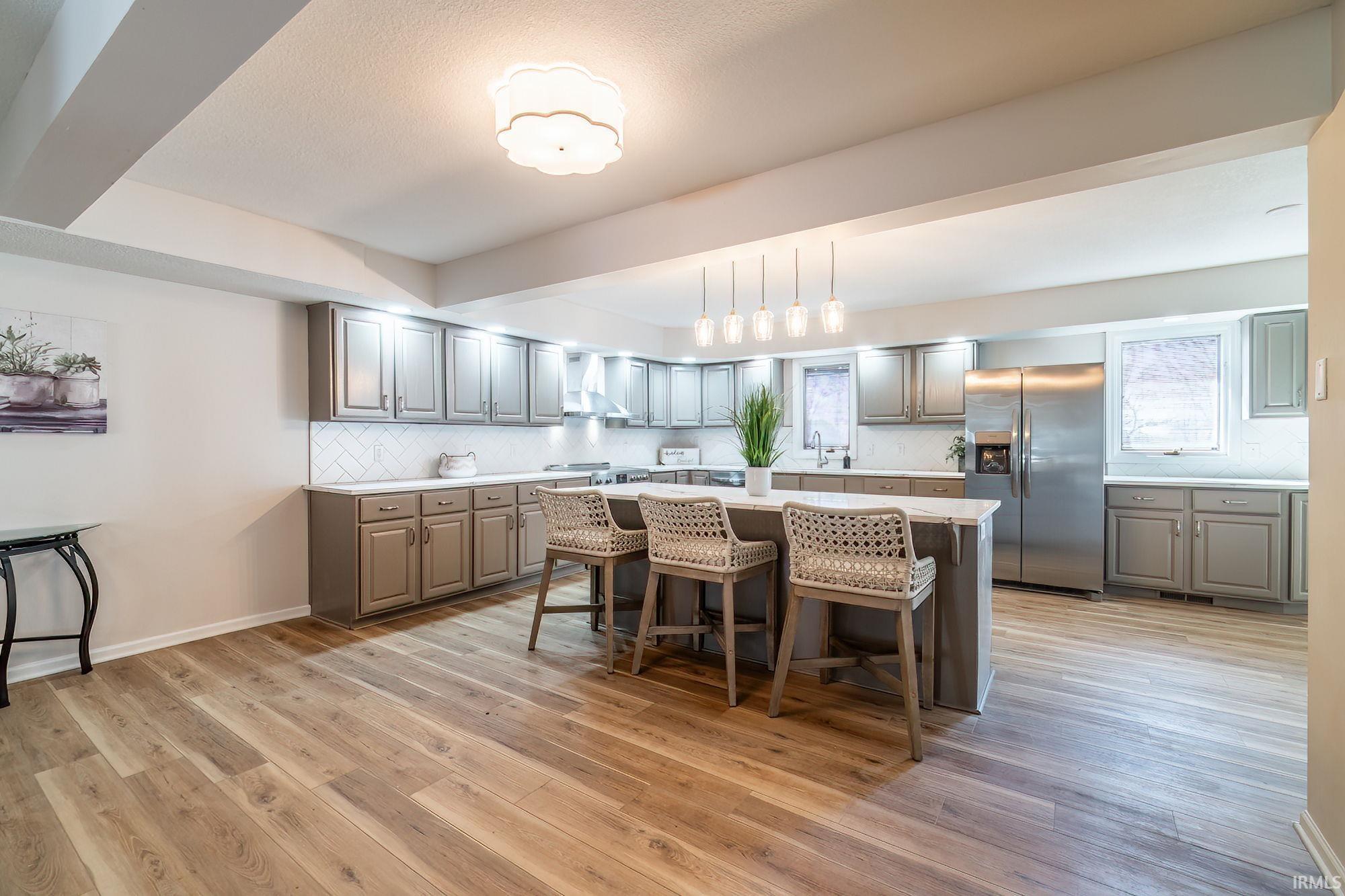Kitchen featuring a kitchen breakfast bar, stainless steel refrigerator with ice dispenser, gray cabinetry, a kitchen island, and backsplash