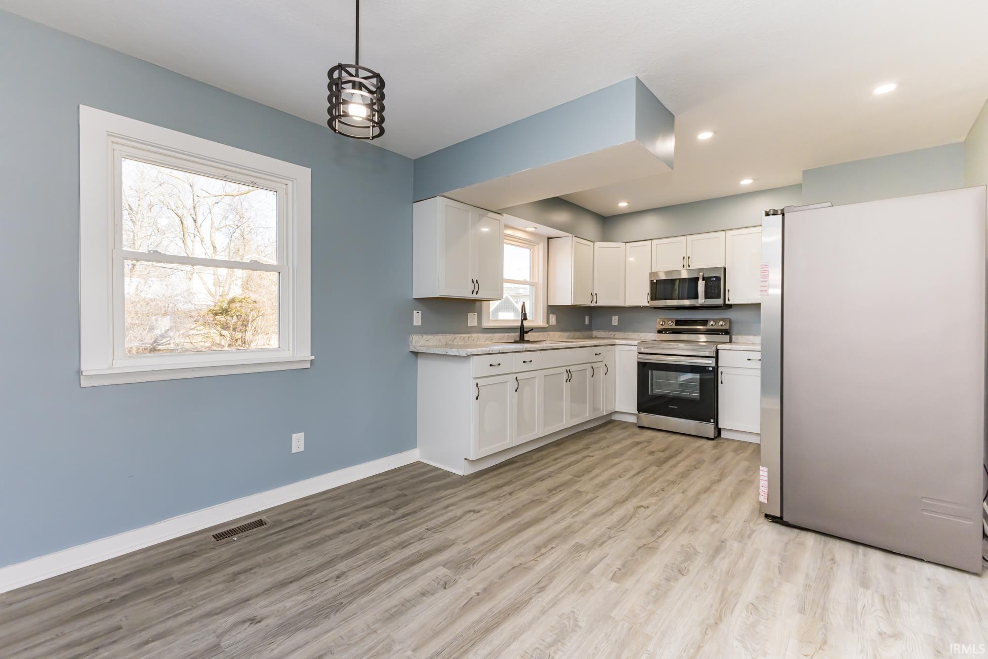 Kitchen with stainless steel appliances, white cabinetry, light wood-style flooring, and decorative light fixtures