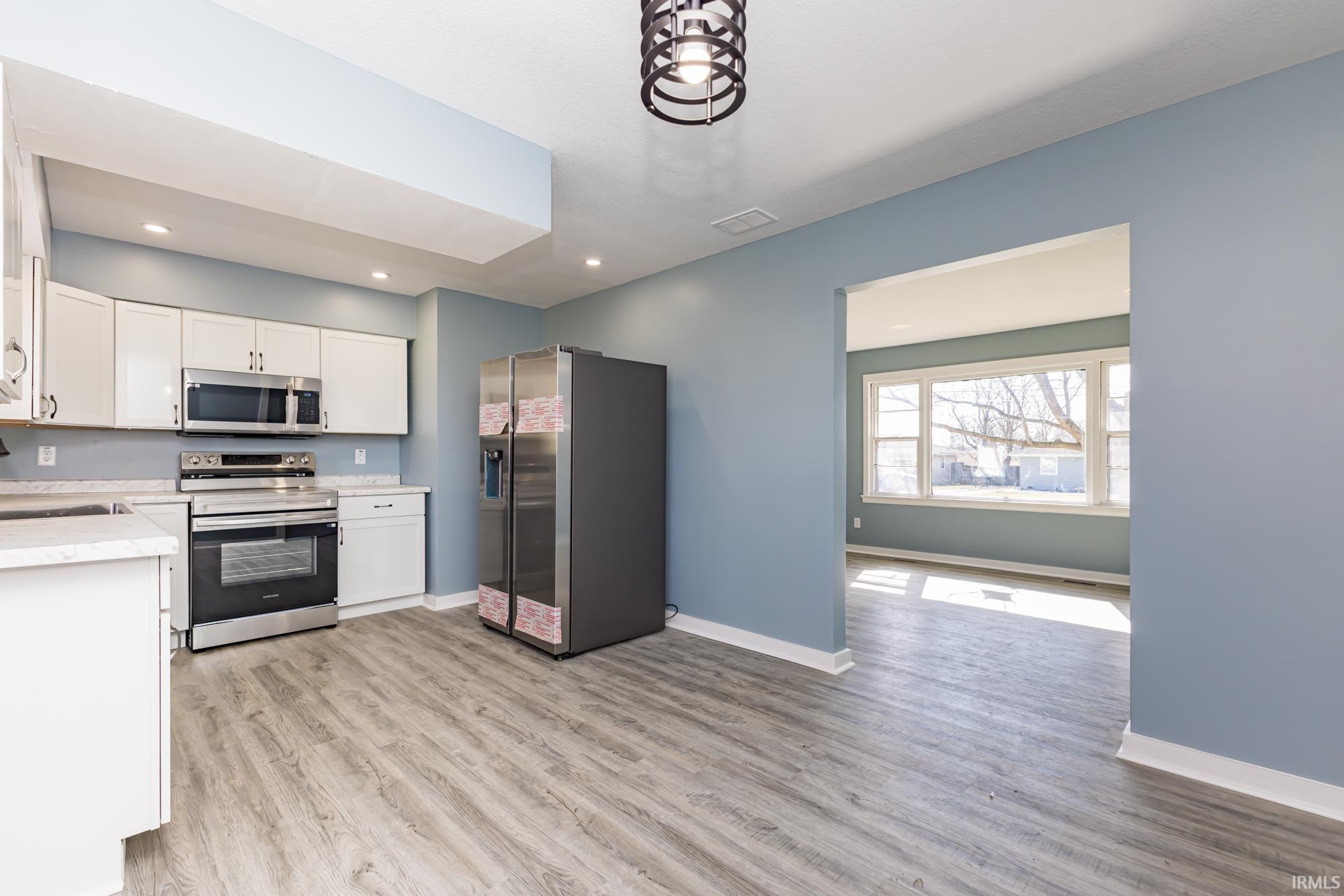 Kitchen with light countertops, stainless steel appliances, white cabinets, light wood-style floors, and recessed lighting