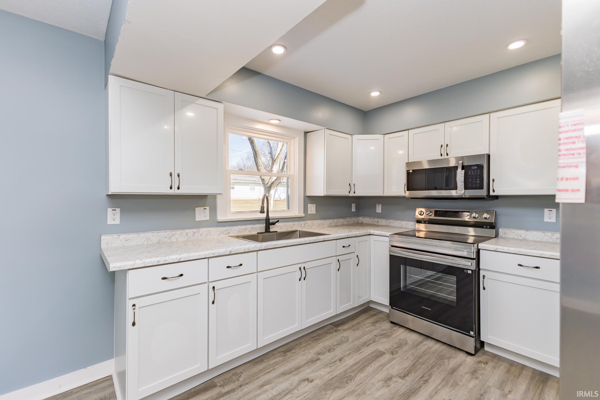 Kitchen with stainless steel appliances, white cabinetry, light wood-style floors, and recessed lighting