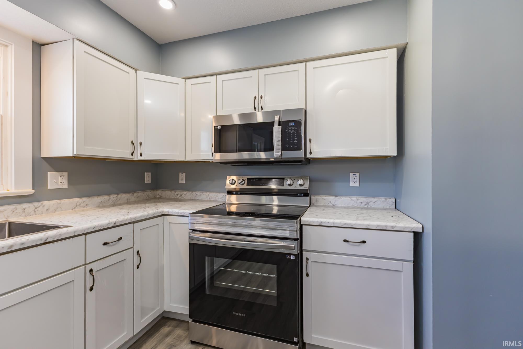 Kitchen featuring stainless steel appliances, white cabinetry, dark wood-style floors, and light stone countertops