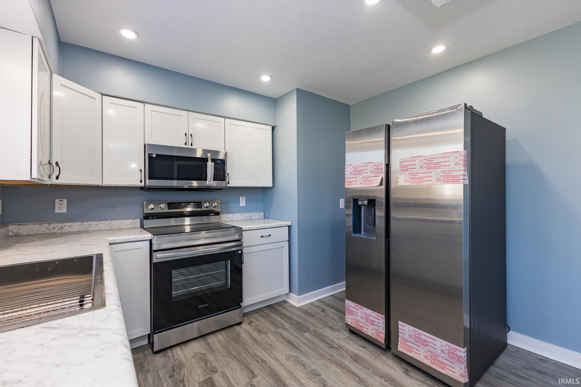 Kitchen with stainless steel appliances, white cabinetry, light wood finished floors, and recessed lighting
