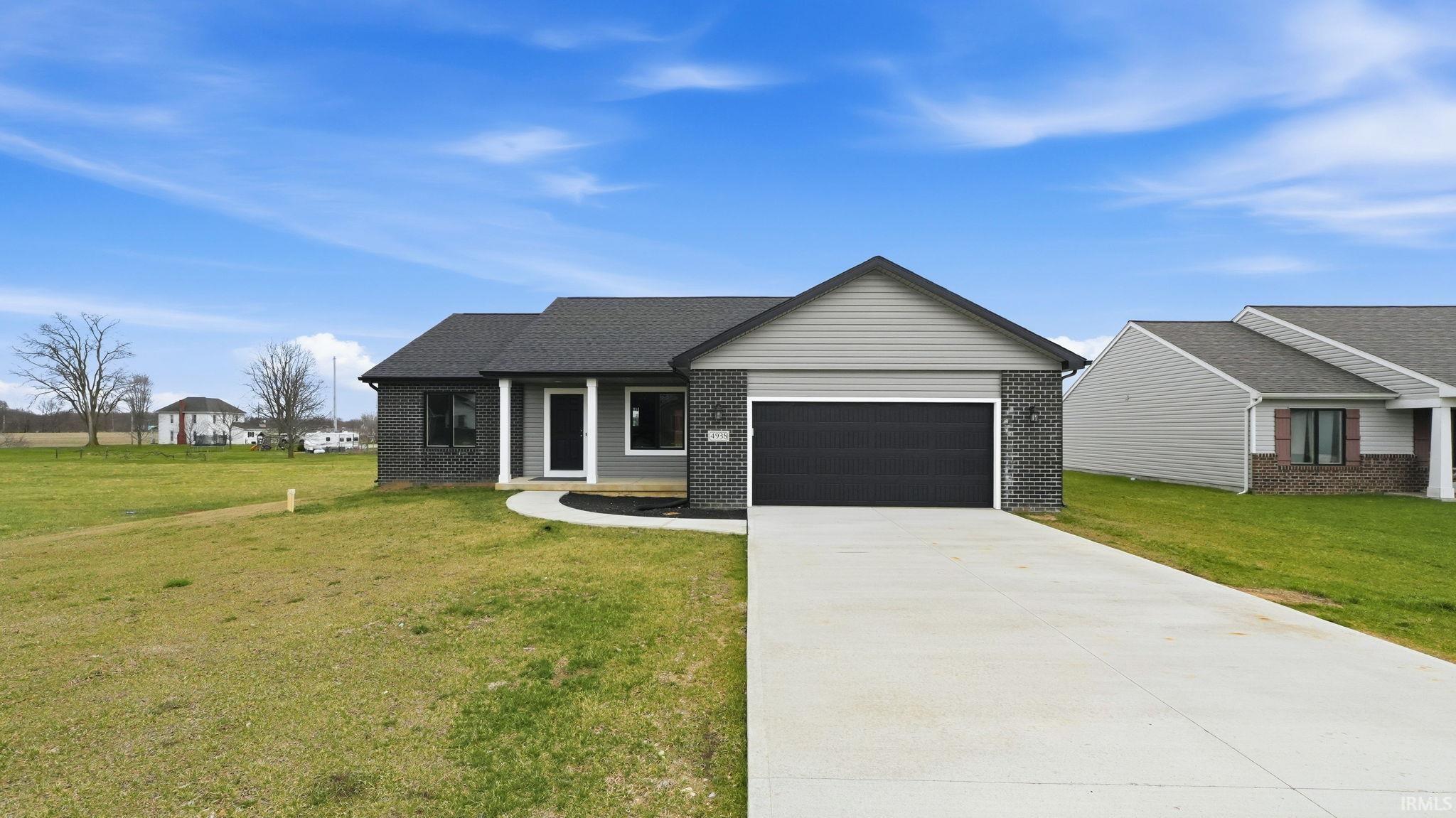 View of front facade with concrete driveway, a front yard, brick siding, a garage, and covered porch