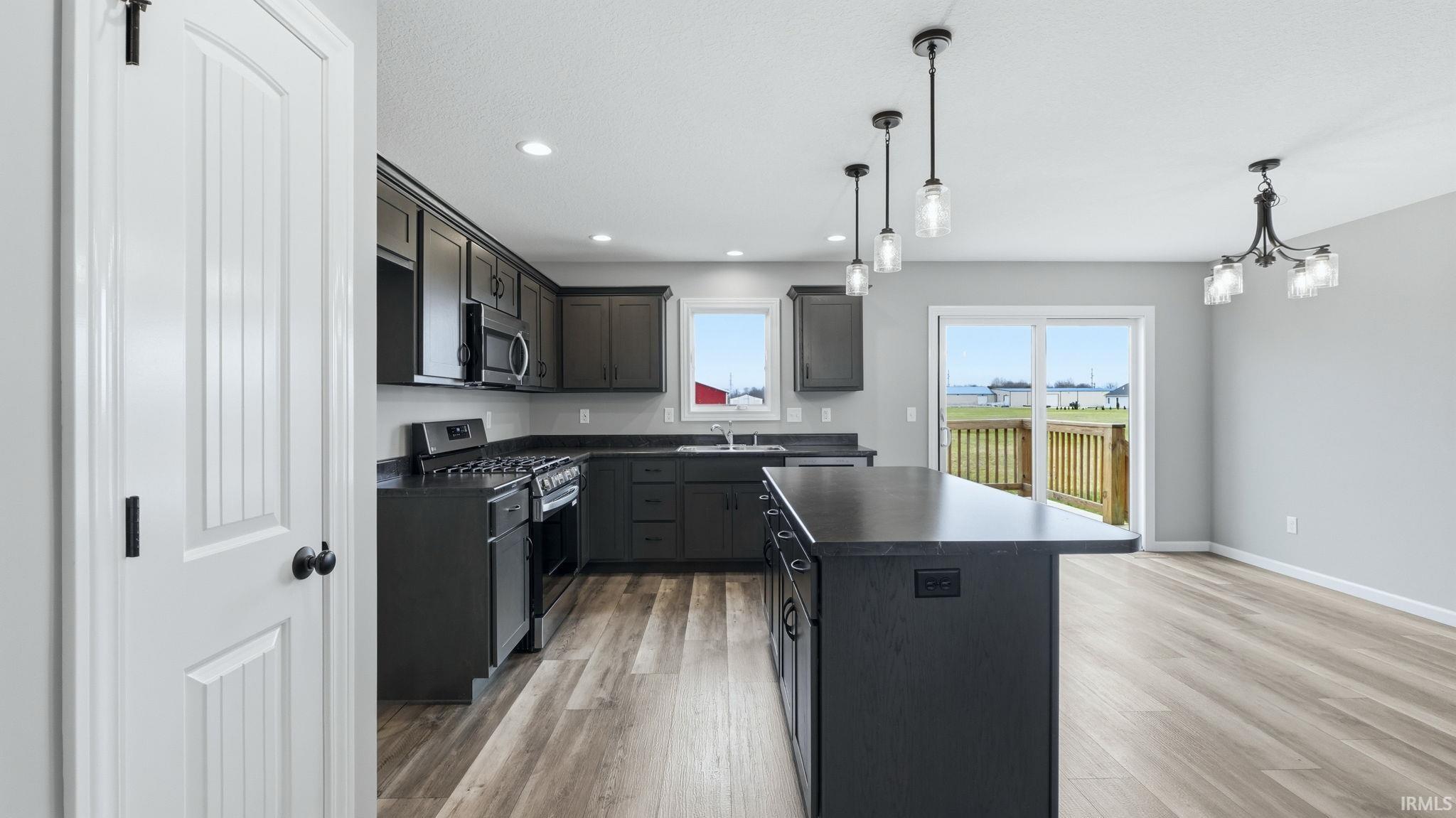 Kitchen featuring dark countertops, stainless steel appliances, a kitchen island, light wood finished floors, and hanging lights