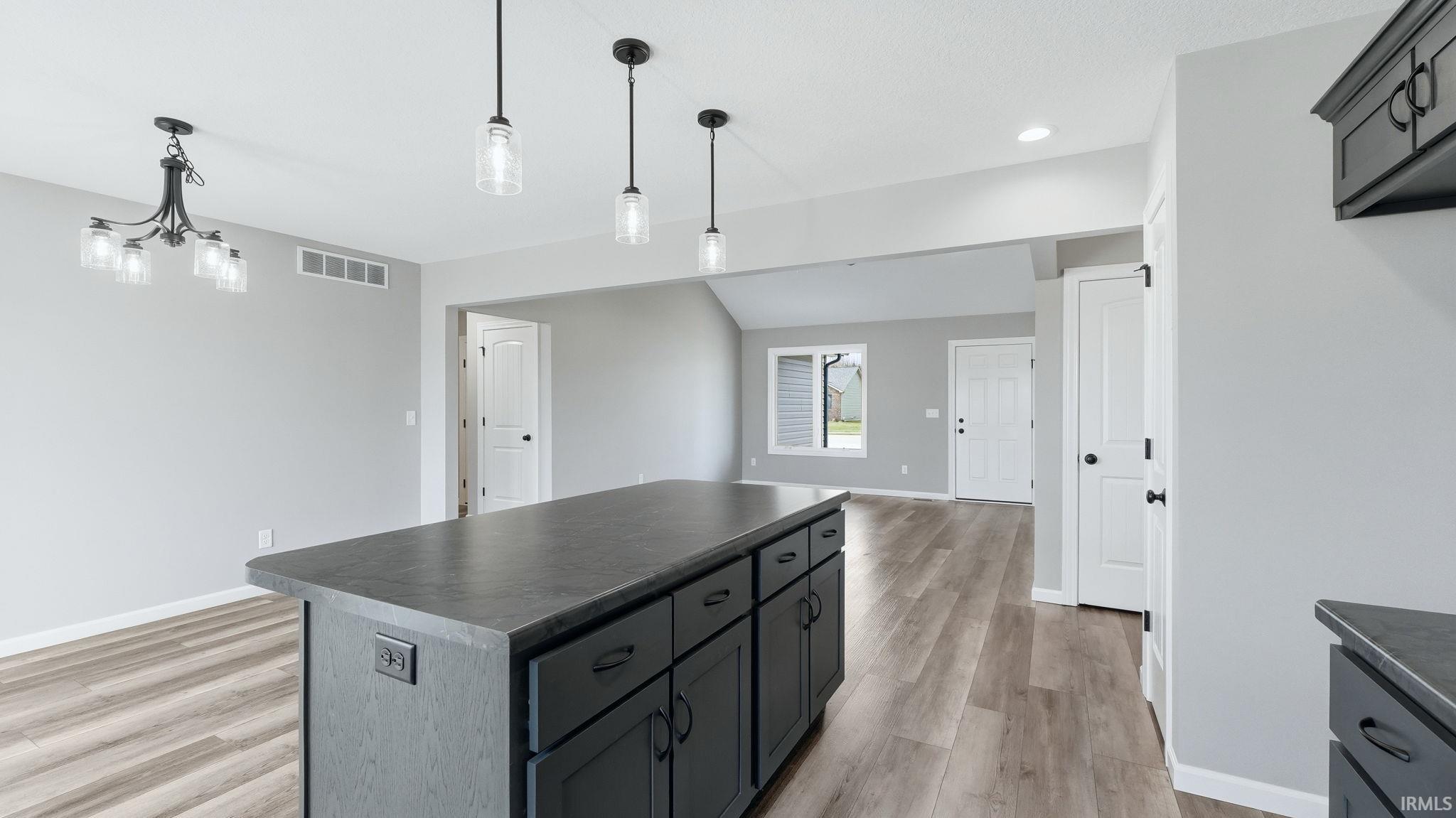 Kitchen featuring dark countertops, a kitchen island, pendant lighting, light wood-type flooring, and vaulted ceiling