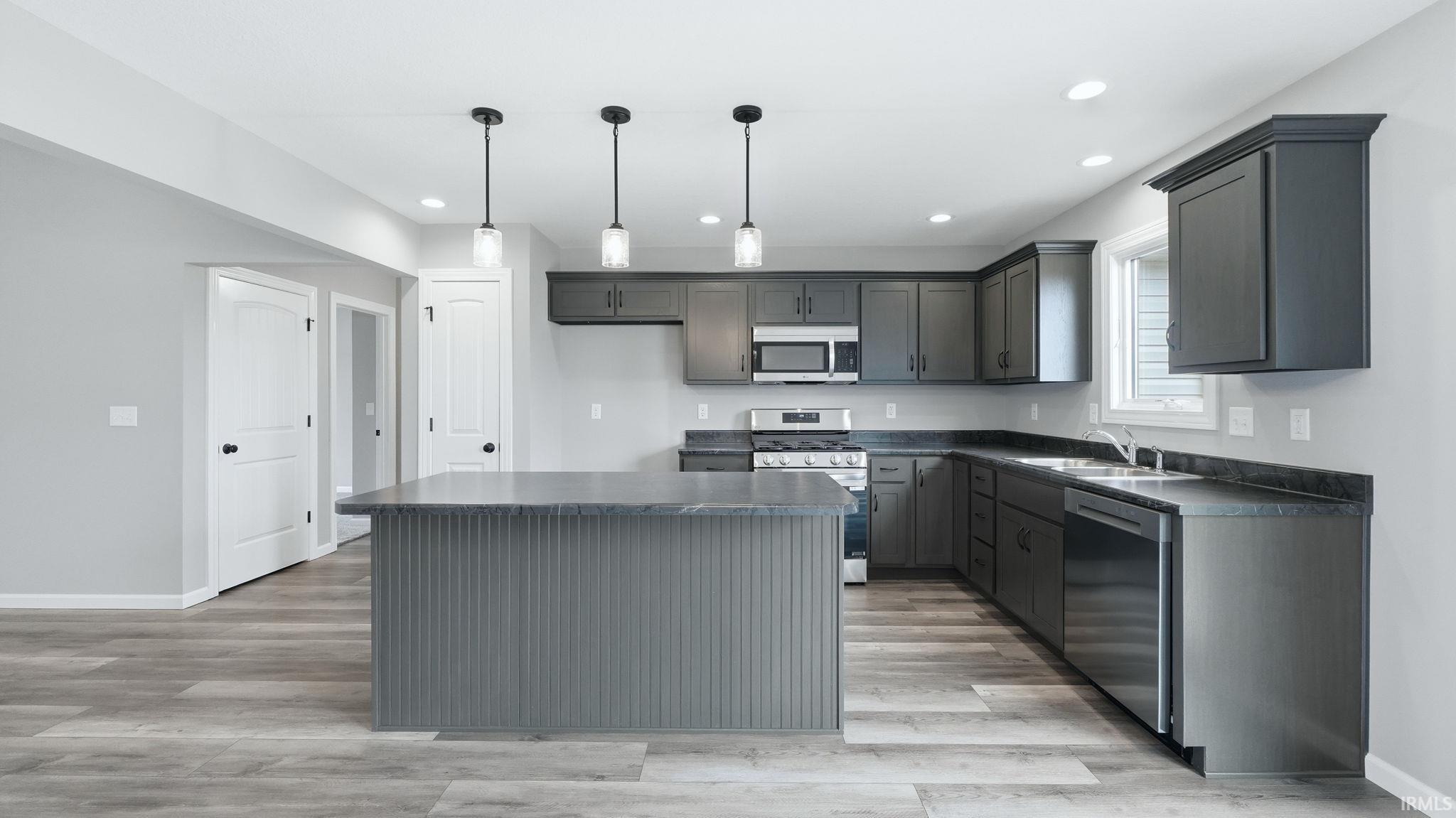 Kitchen with dark countertops, stainless steel appliances, a kitchen island, light wood-style floors, and hanging light fixtures
