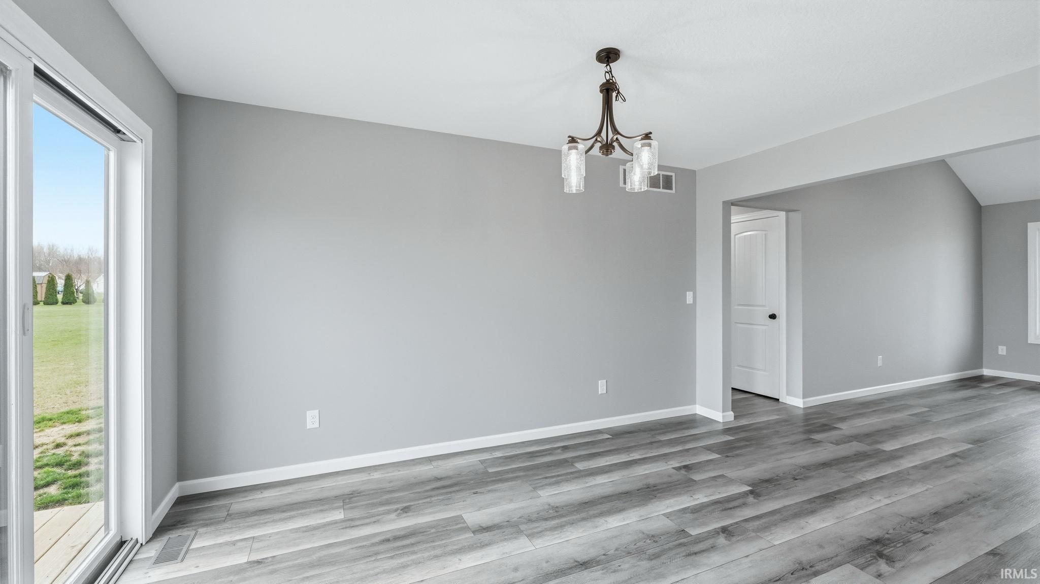Spare room with plenty of natural light, suspended lighting, and light wood-type flooring
