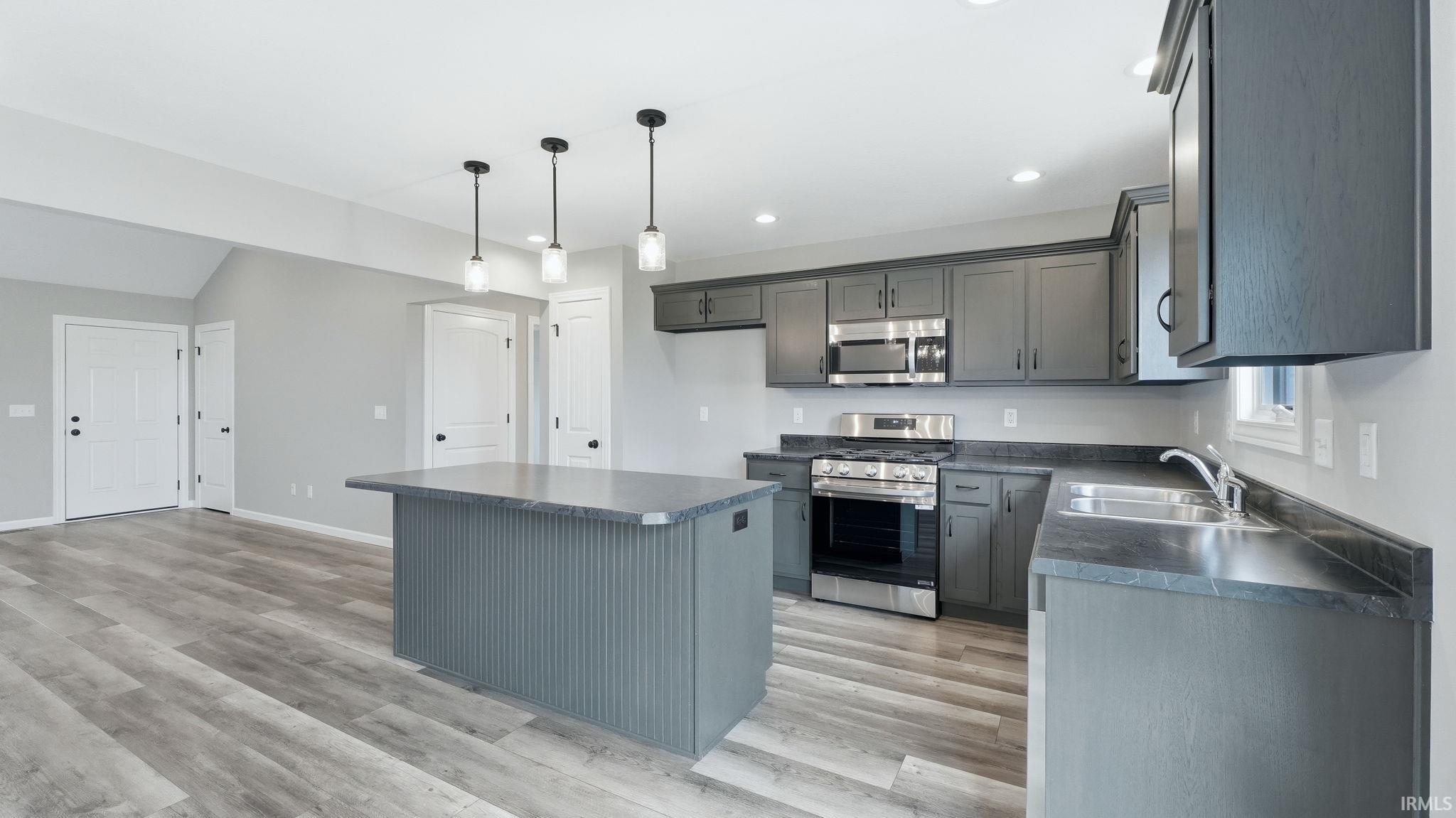Kitchen with dark countertops, stainless steel appliances, a center island, and light wood finished floors