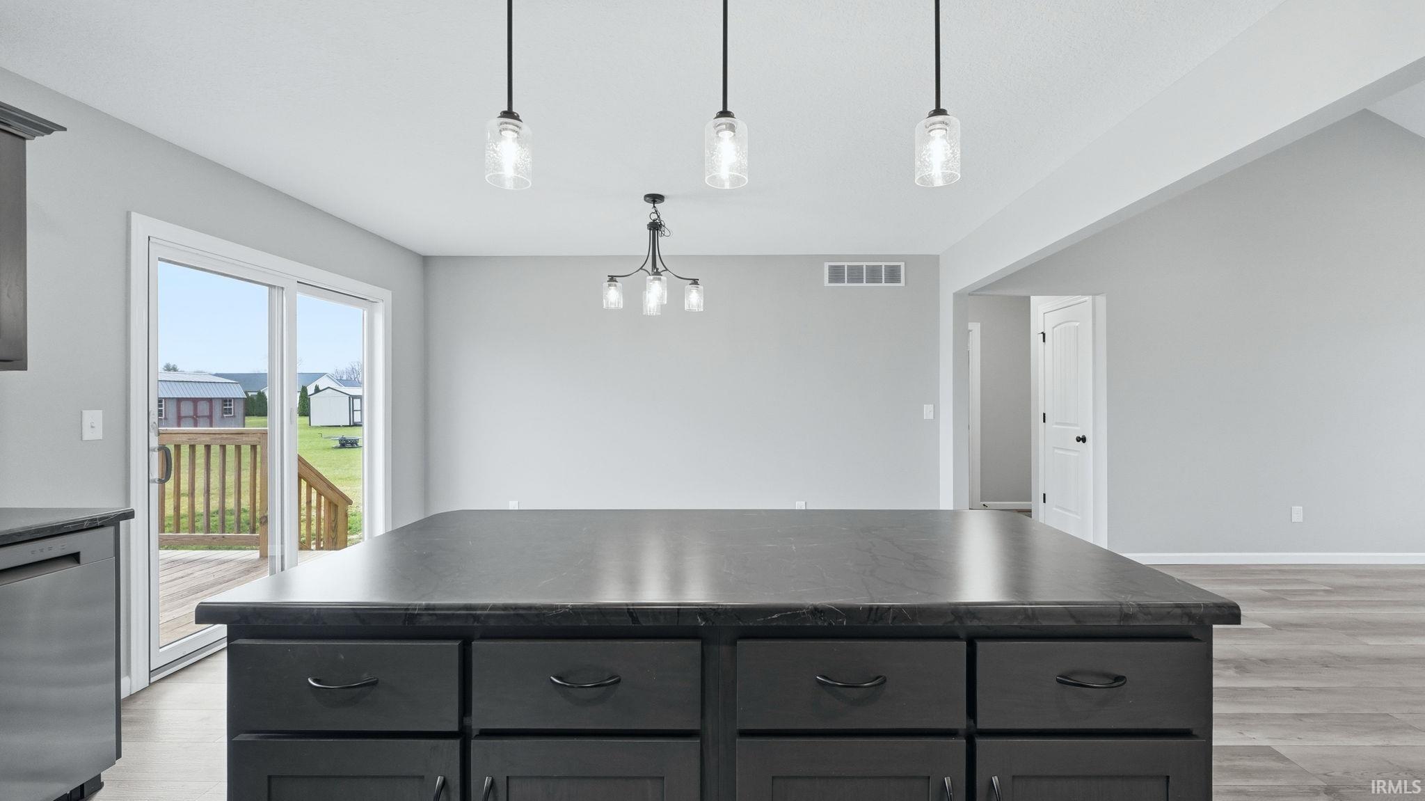 Kitchen with a center island, dark countertops, dishwasher, pendant lighting, and light wood-type flooring