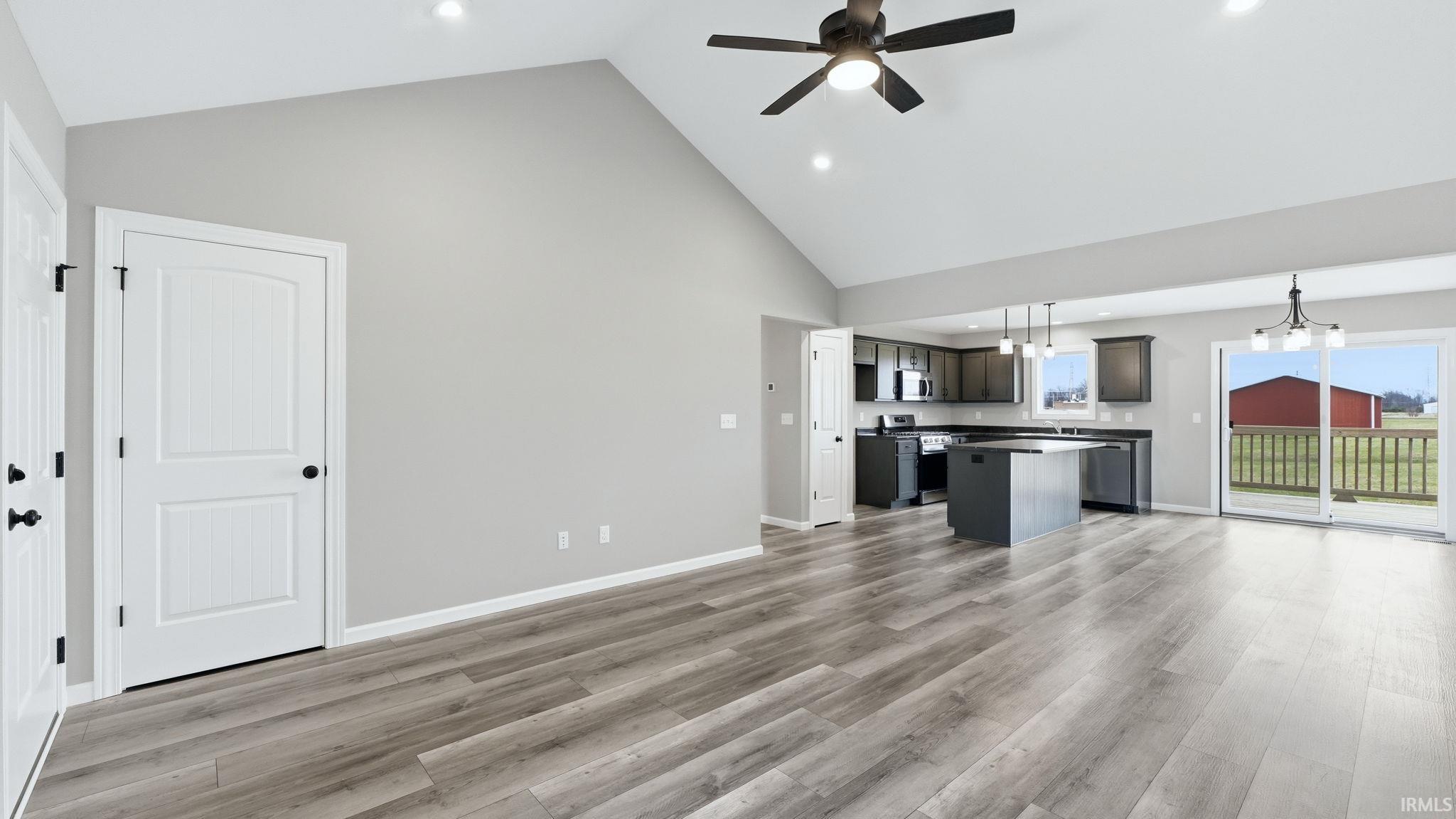 Unfurnished living room featuring a ceiling fan, lofted ceiling, hanging lights, and light wood-type flooring