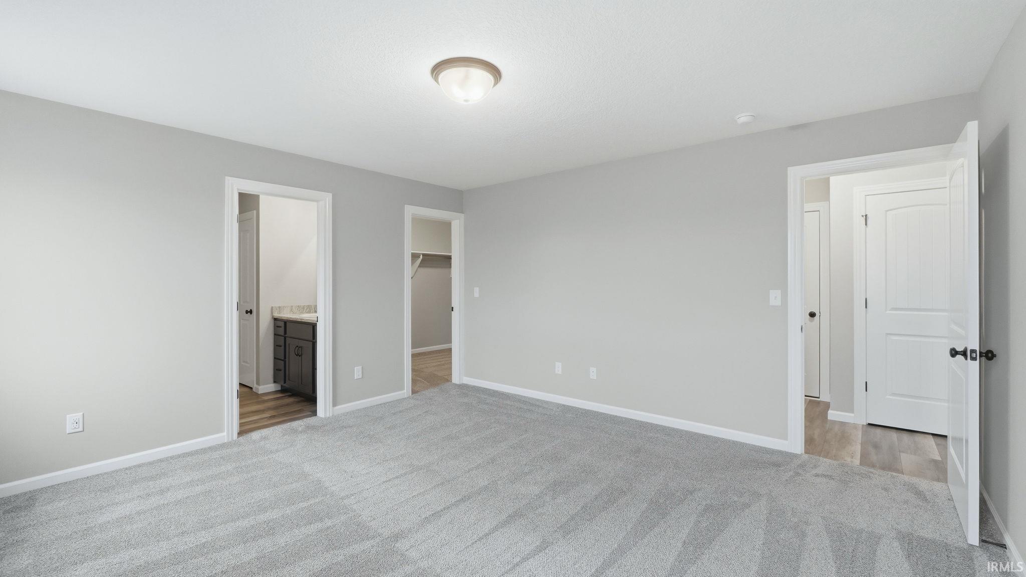 Unfurnished bedroom with a walk in closet, light carpet, and ensuite bathroom