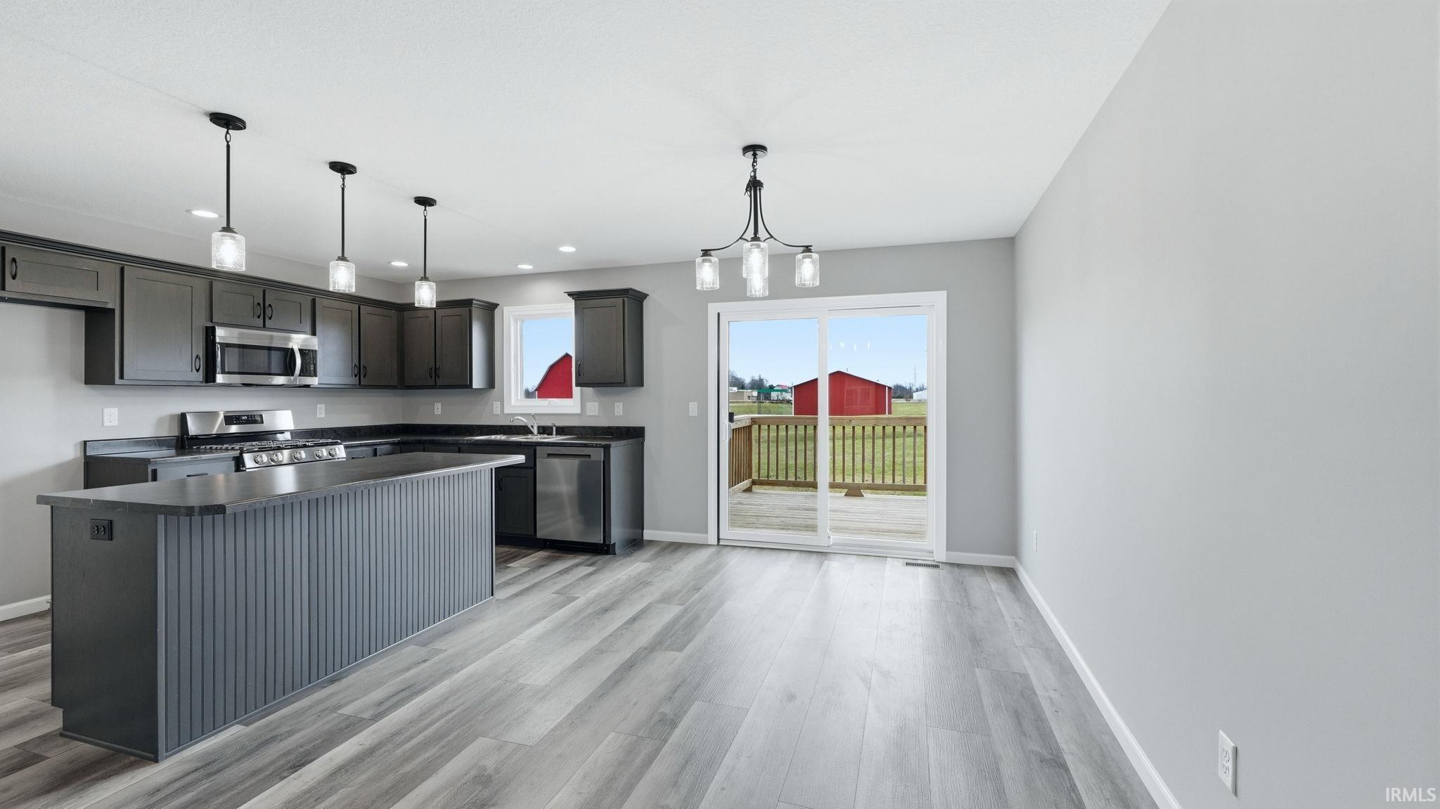 Kitchen with dark countertops, a center island, stainless steel appliances, and light wood-style floors