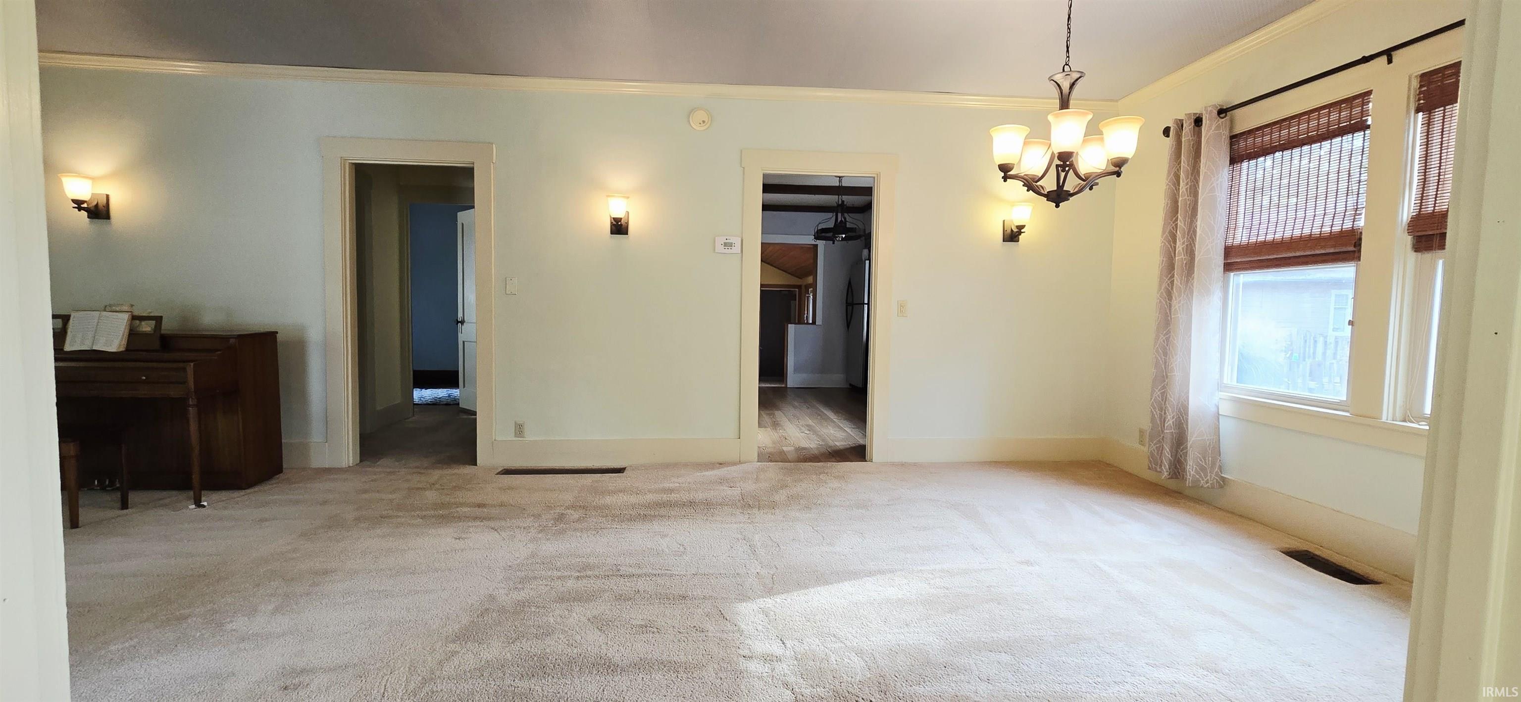 Unfurnished dining area with light colored carpet, crown molding, and hanging lights