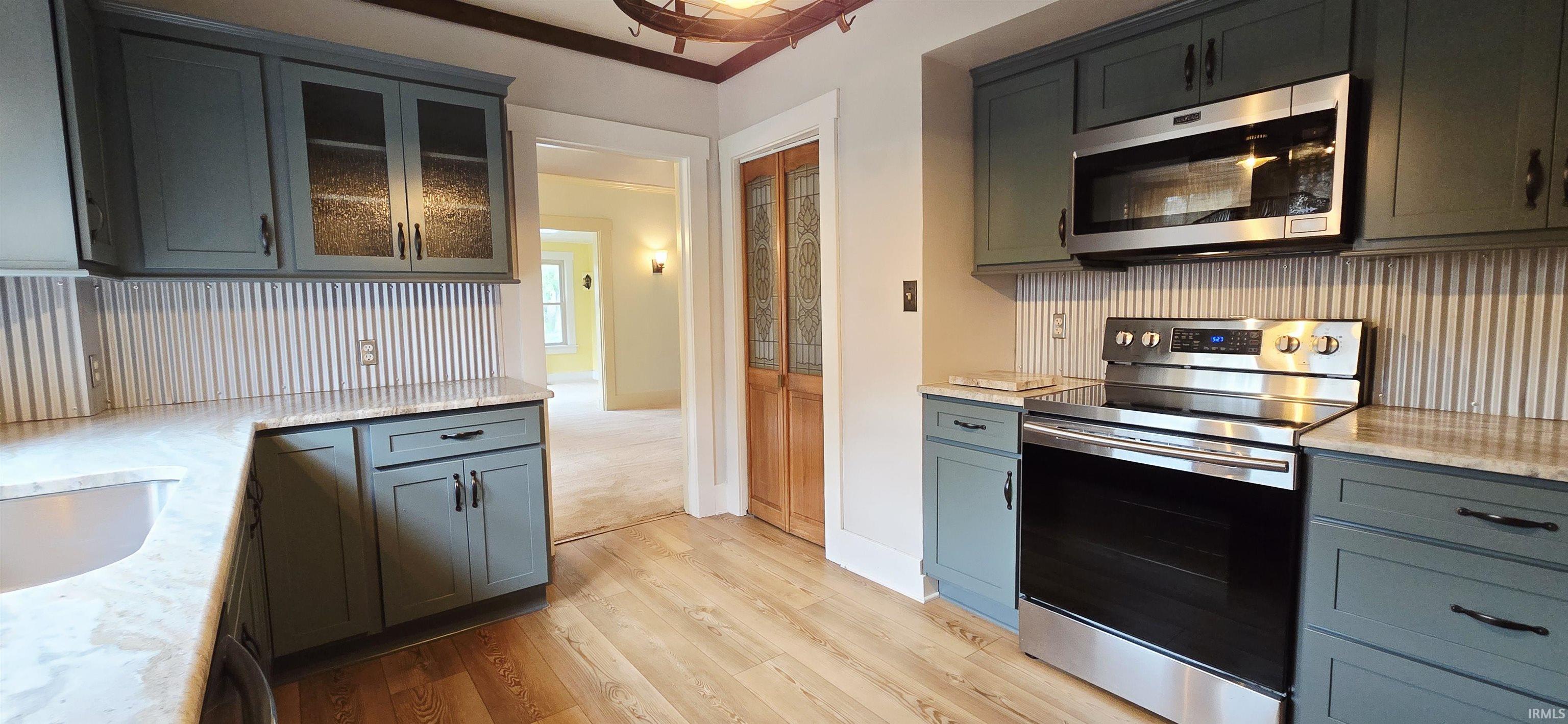 Kitchen featuring stainless steel appliances, light stone counters, glass insert cabinets, and light wood-type flooring