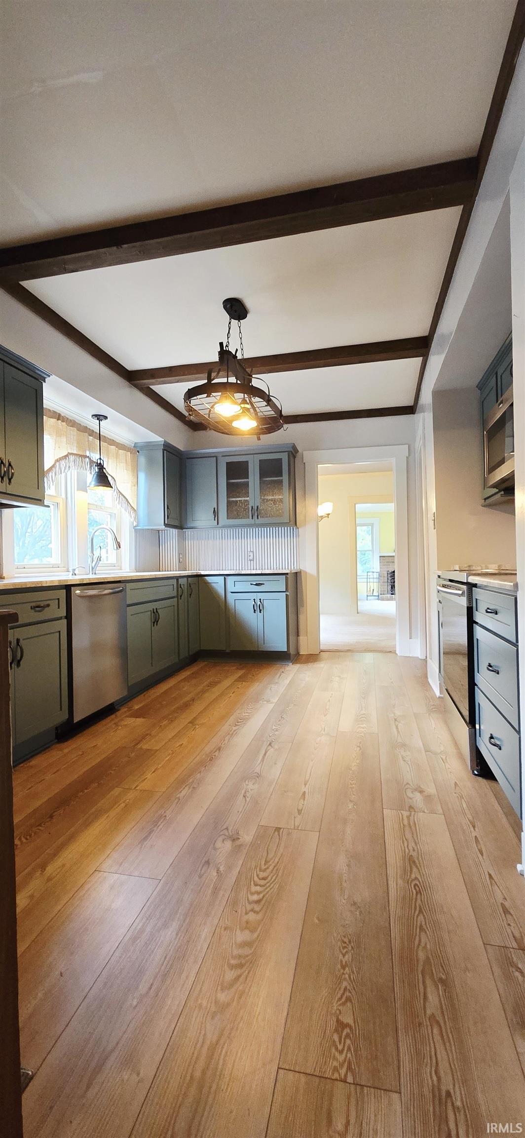 Kitchen featuring light wood-type flooring, beam ceiling, glass fronted cabinets, light countertops, and stainless steel appliances