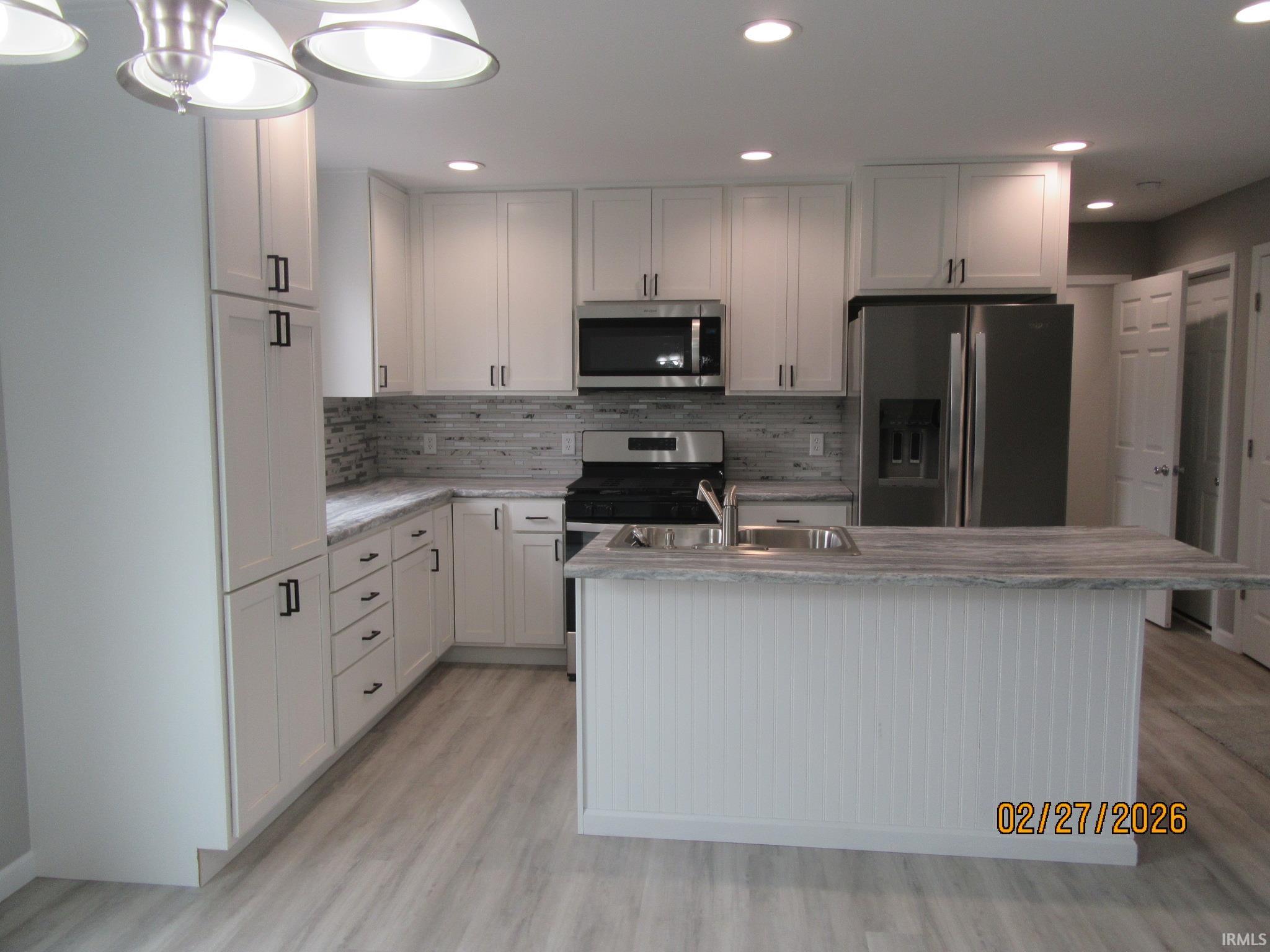 Kitchen featuring stainless steel appliances, white cabinets, an island with sink, light wood-type flooring, and recessed lighting