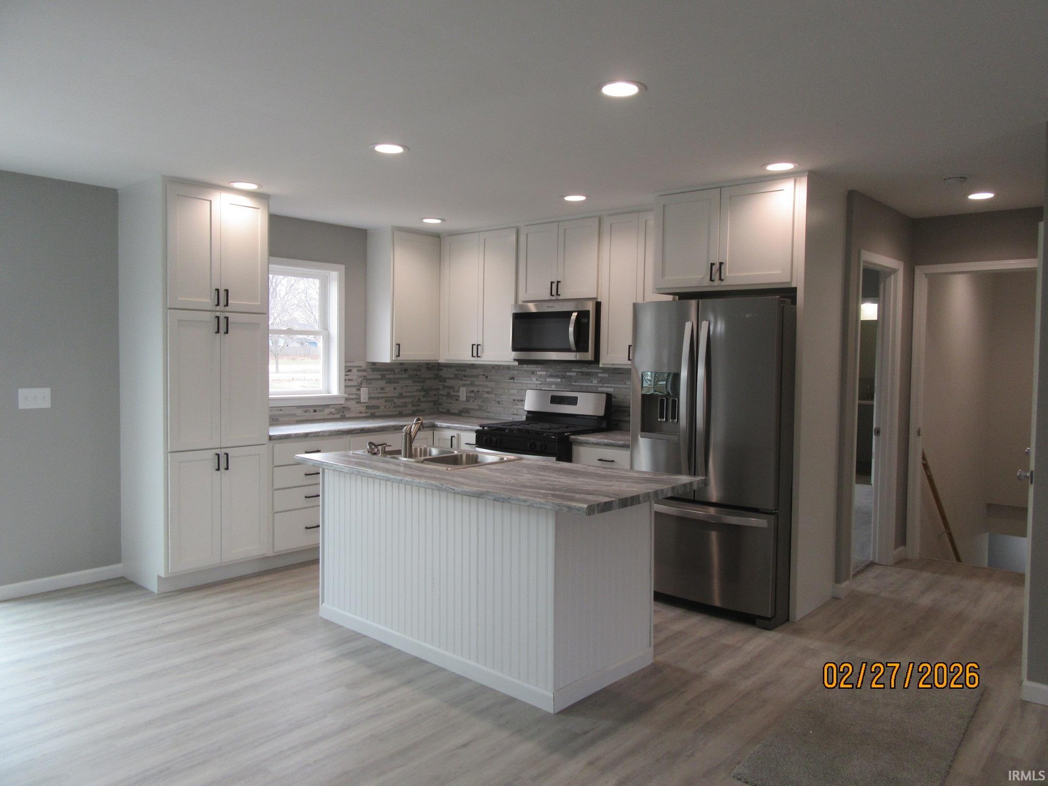 Kitchen featuring stainless steel appliances, an island with sink, white cabinetry, light wood finished floors, and recessed lighting