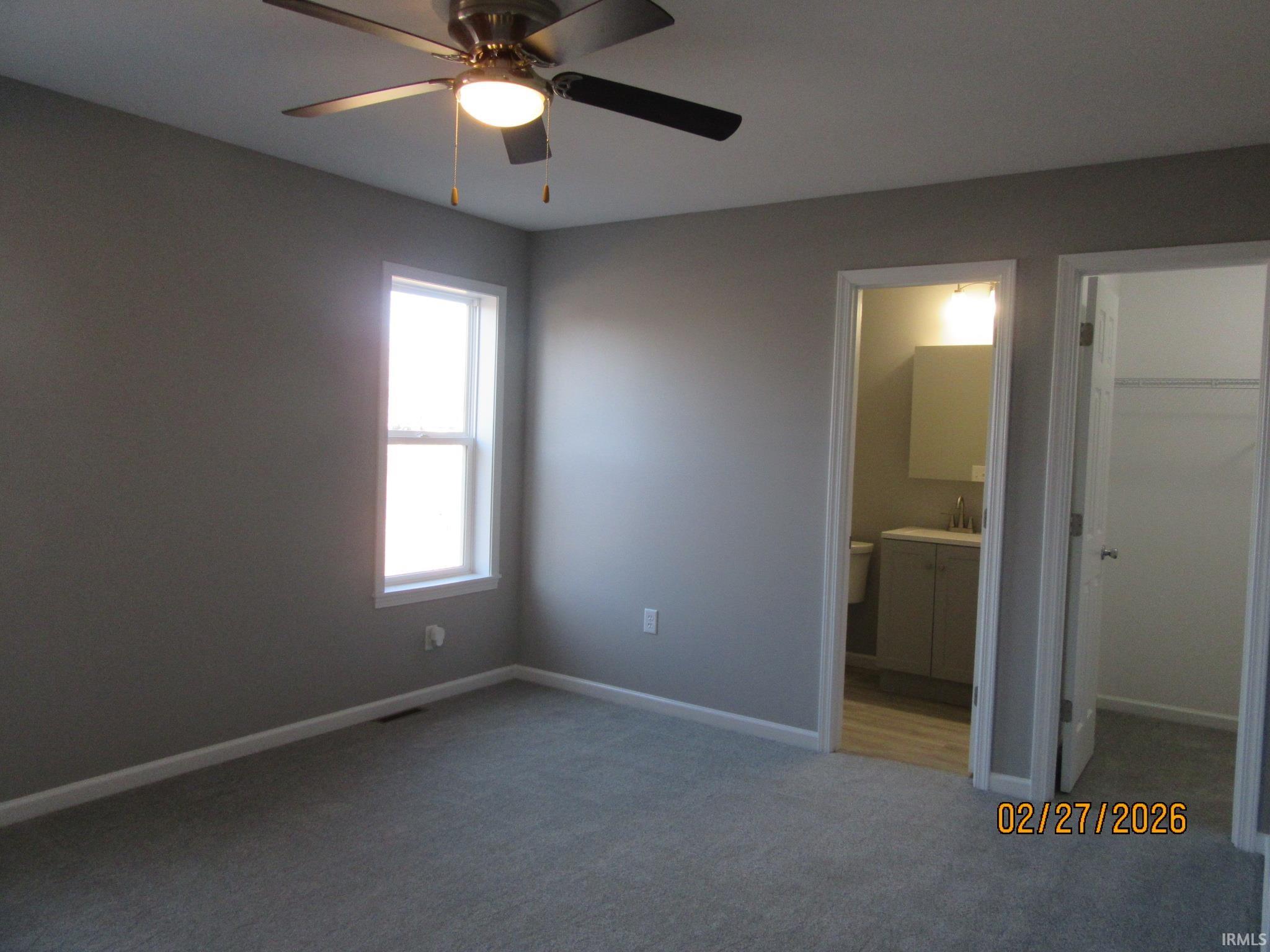 Unfurnished bedroom with a spacious closet, light colored carpet, a ceiling fan, and ensuite bathroom
