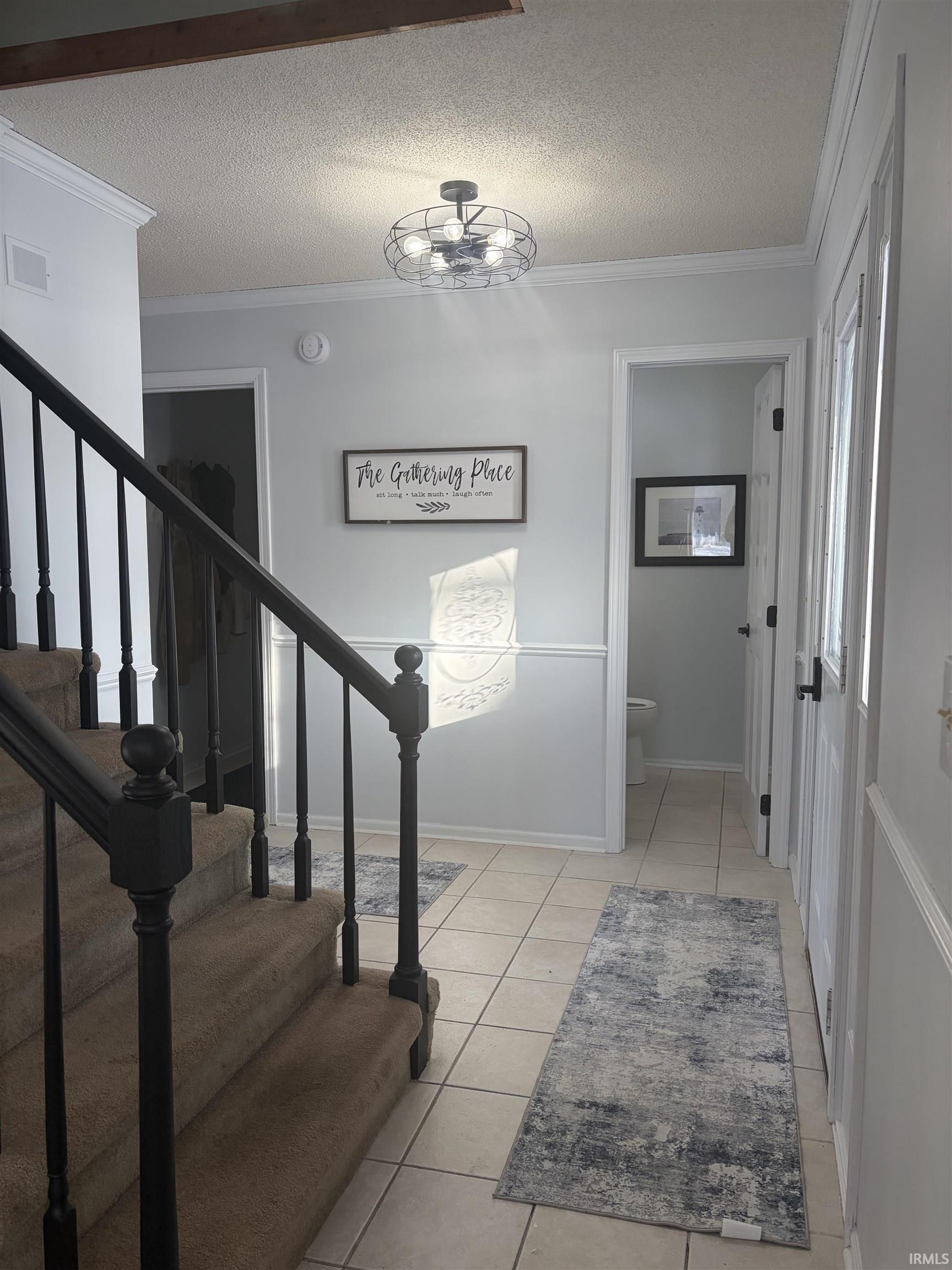 Staircase with a textured ceiling, ornamental molding, and tile patterned floors