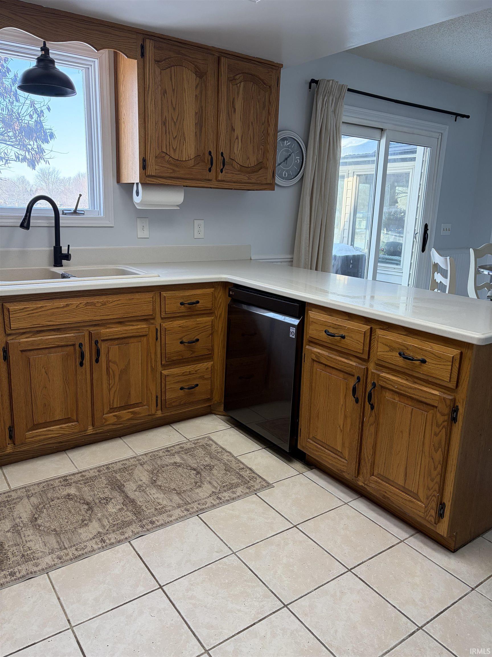 Kitchen with brown cabinets, dishwasher, a peninsula, and light tile patterned flooring