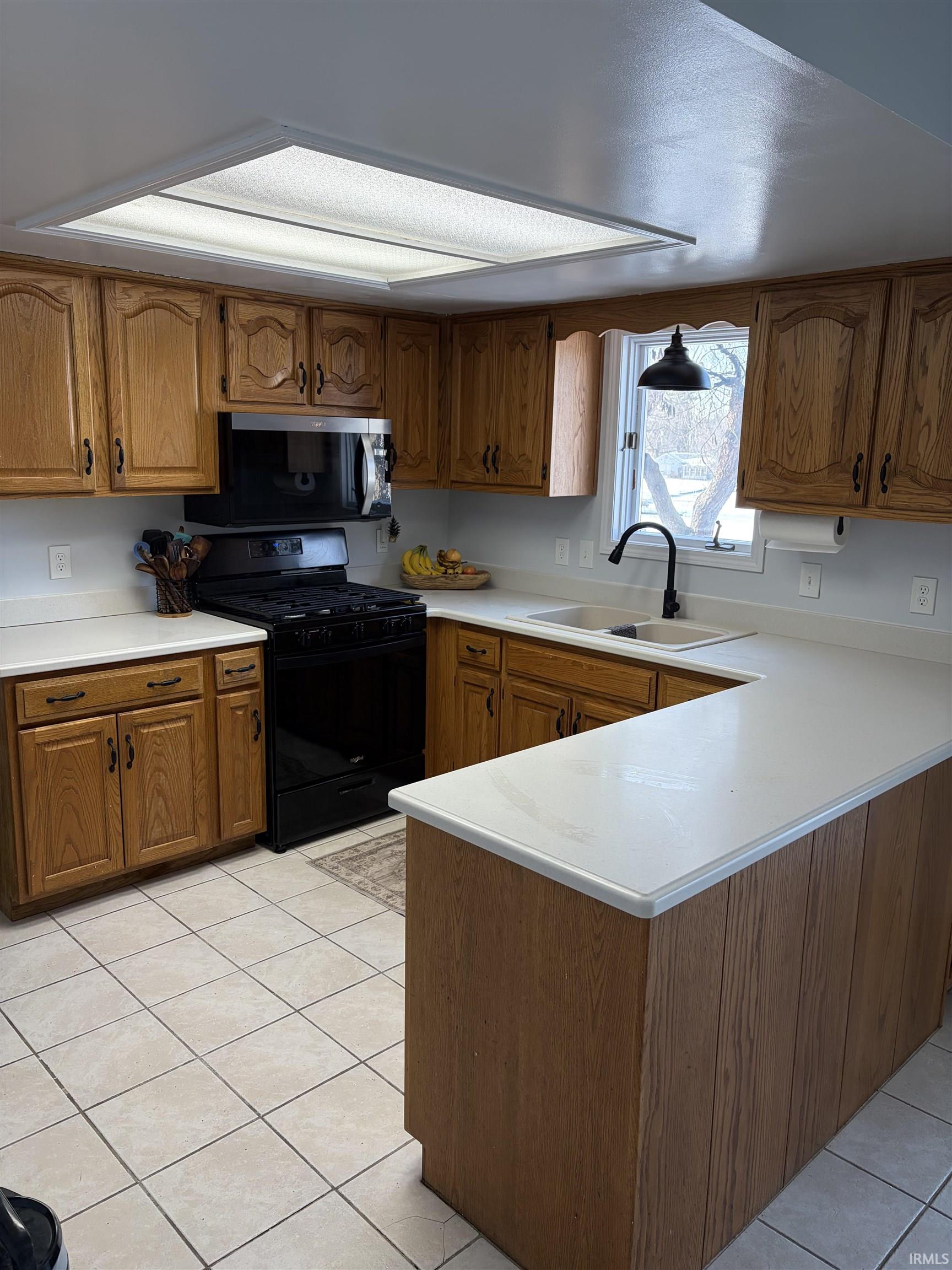 Kitchen featuring brown cabinets, gas stove, light countertops, and a peninsula