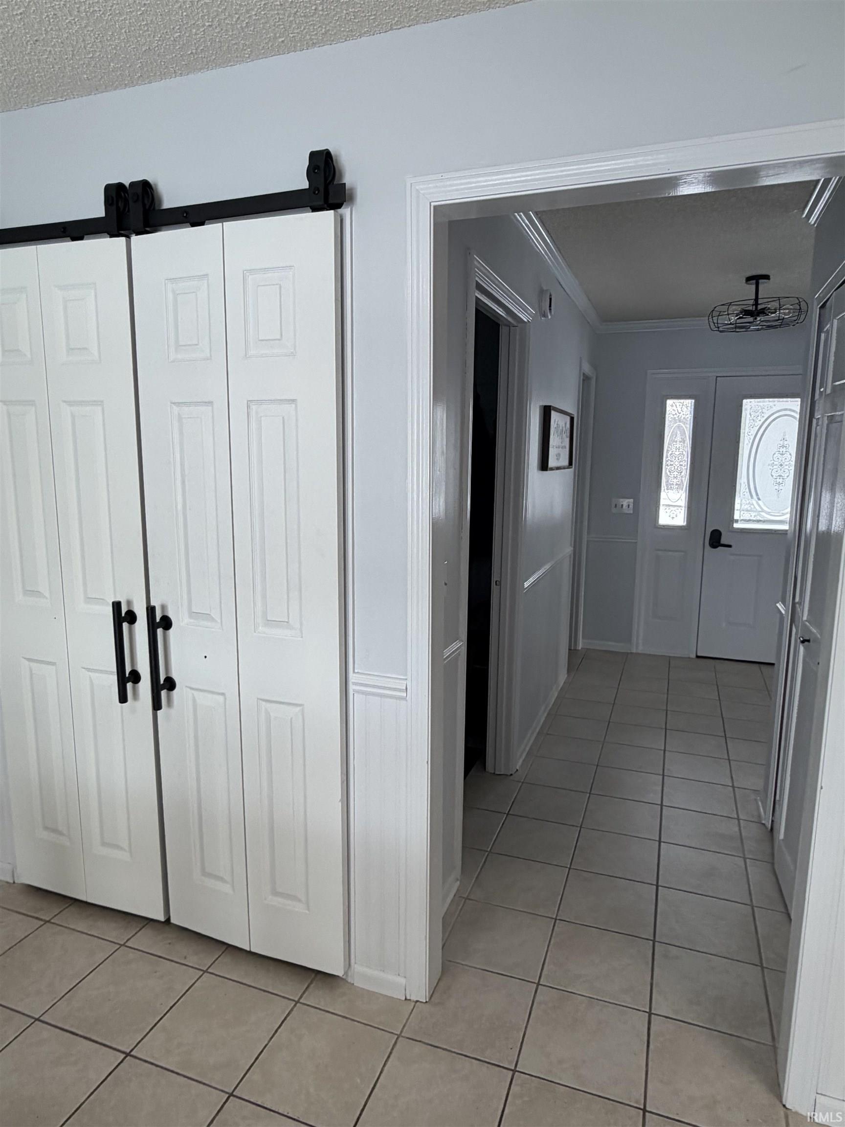 Hallway featuring light tile patterned flooring, a textured ceiling, and crown molding