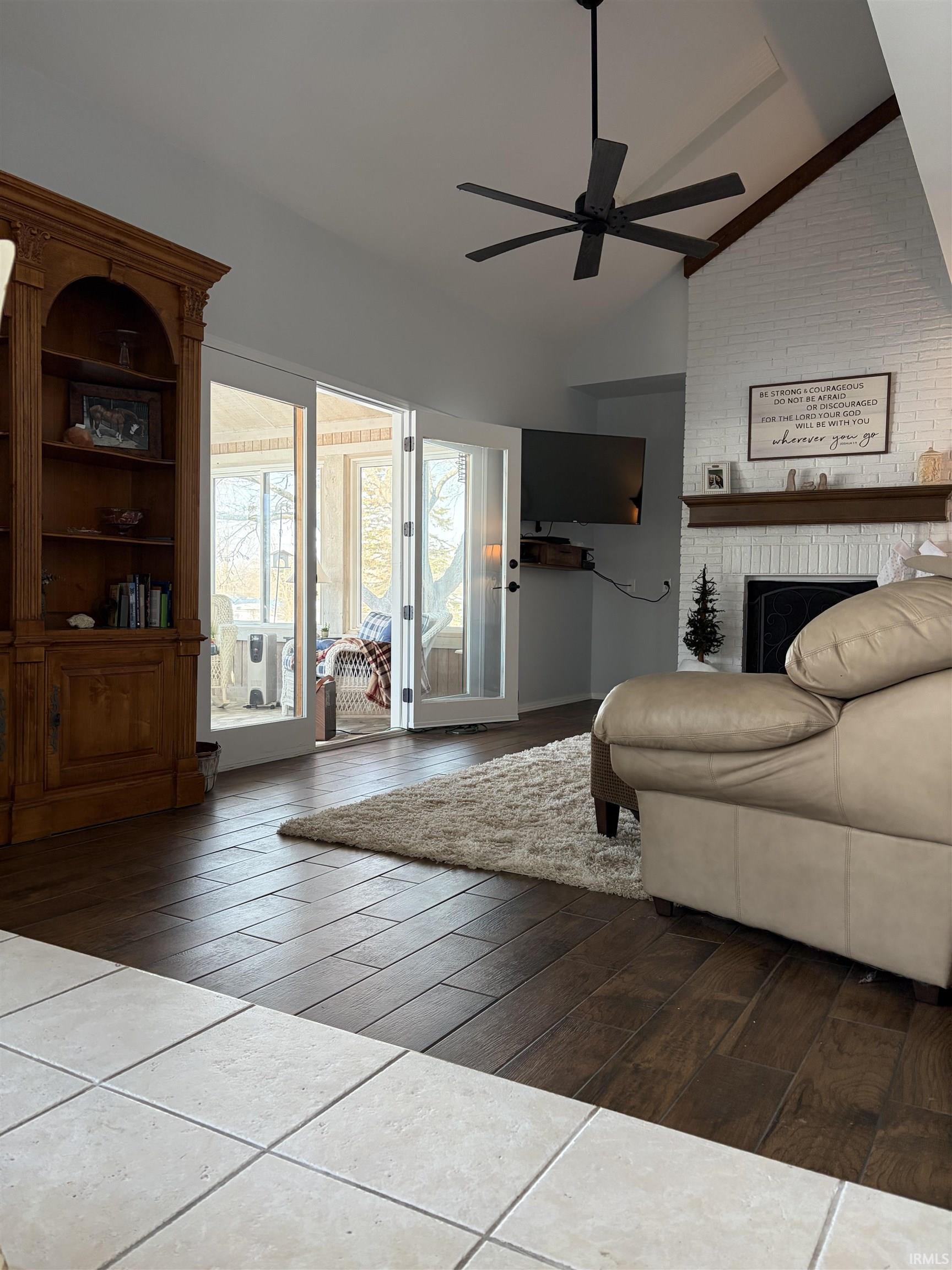 Living area with a brick fireplace, dark wood finished floors, vaulted ceiling, a ceiling fan, and brick wall