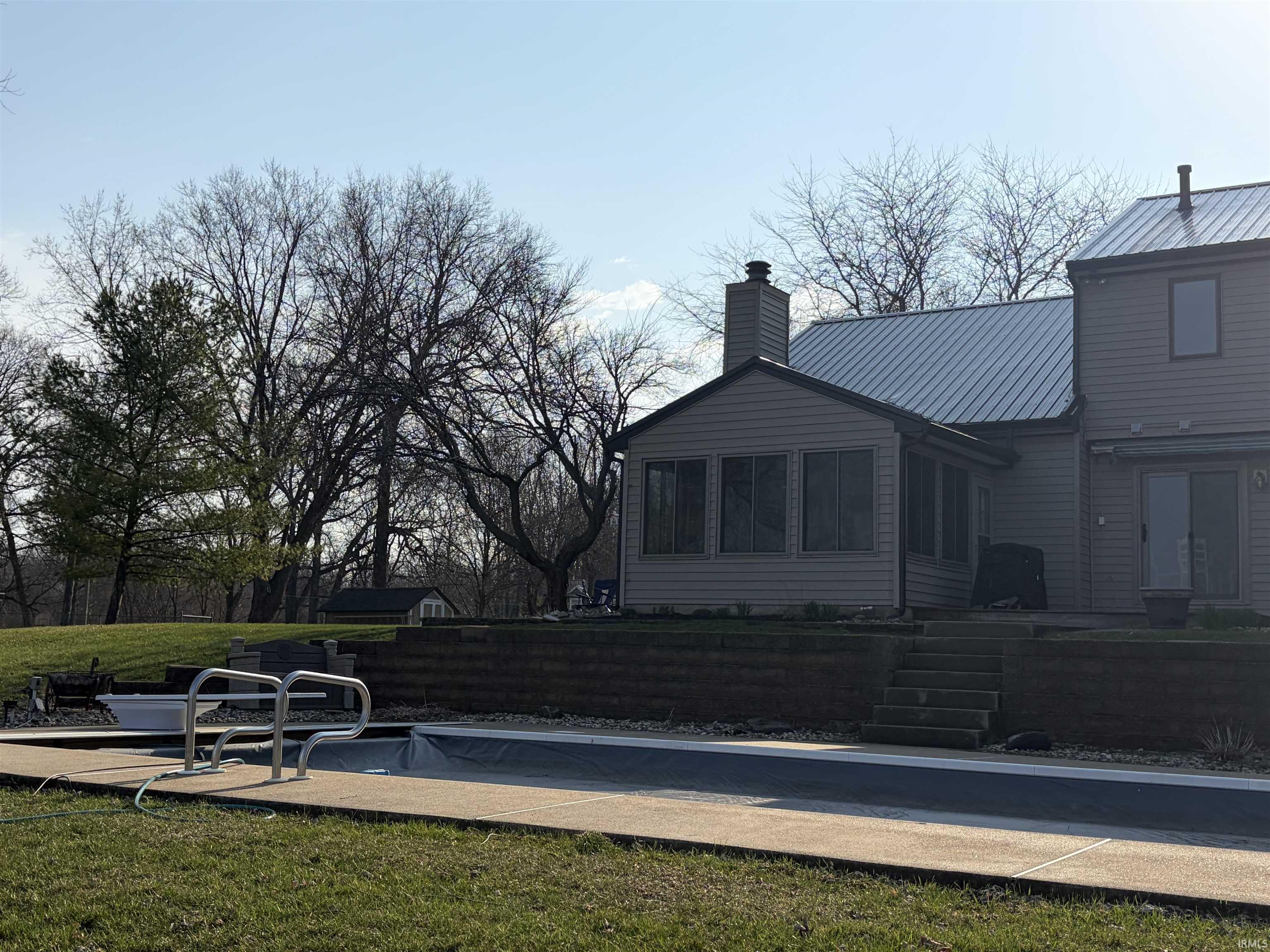 Back of property with a sunroom, a chimney, a metal roof, a patio area, and a lawn
