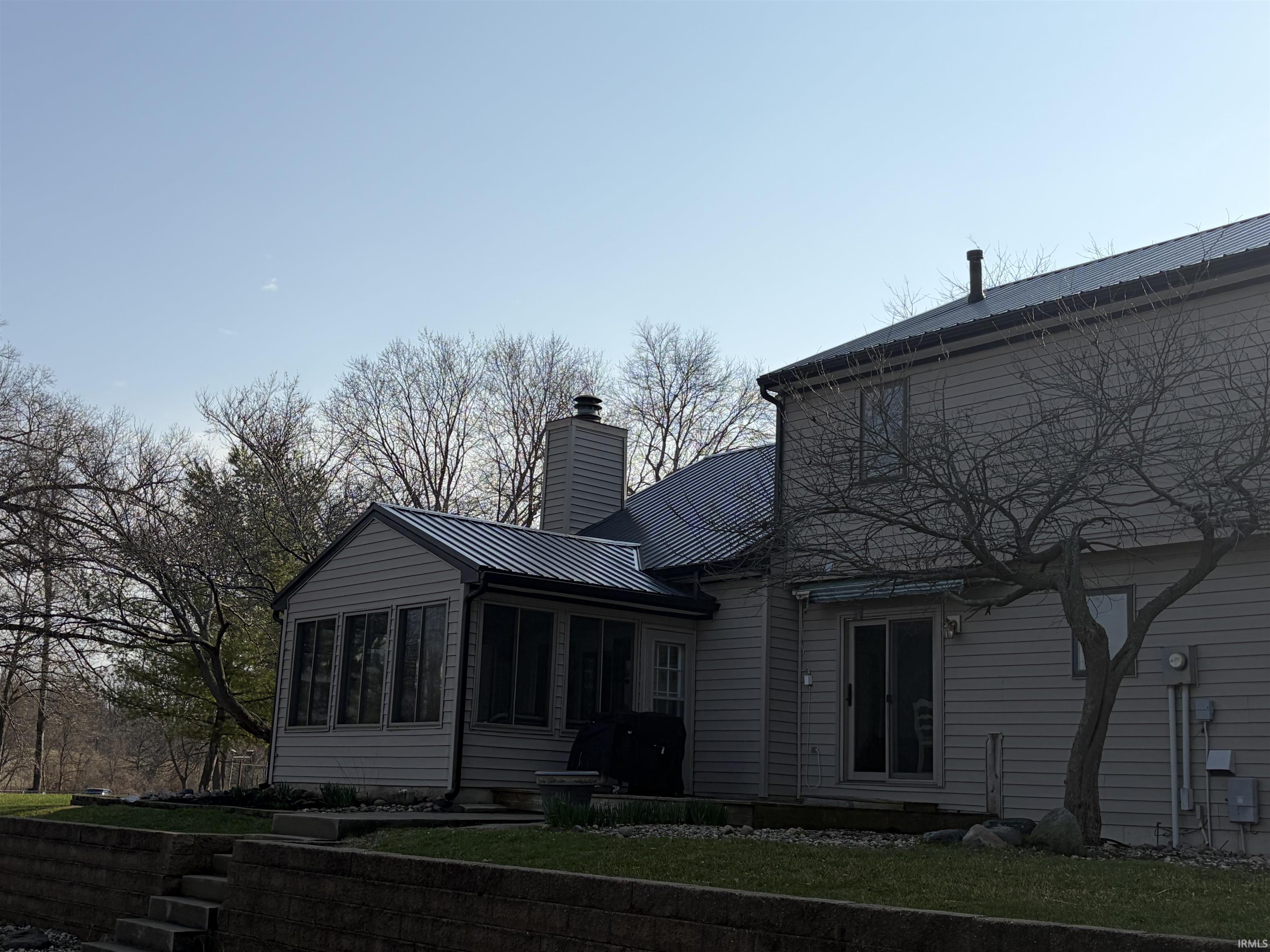 Rear view of property featuring a sunroom, a chimney, and a metal roof