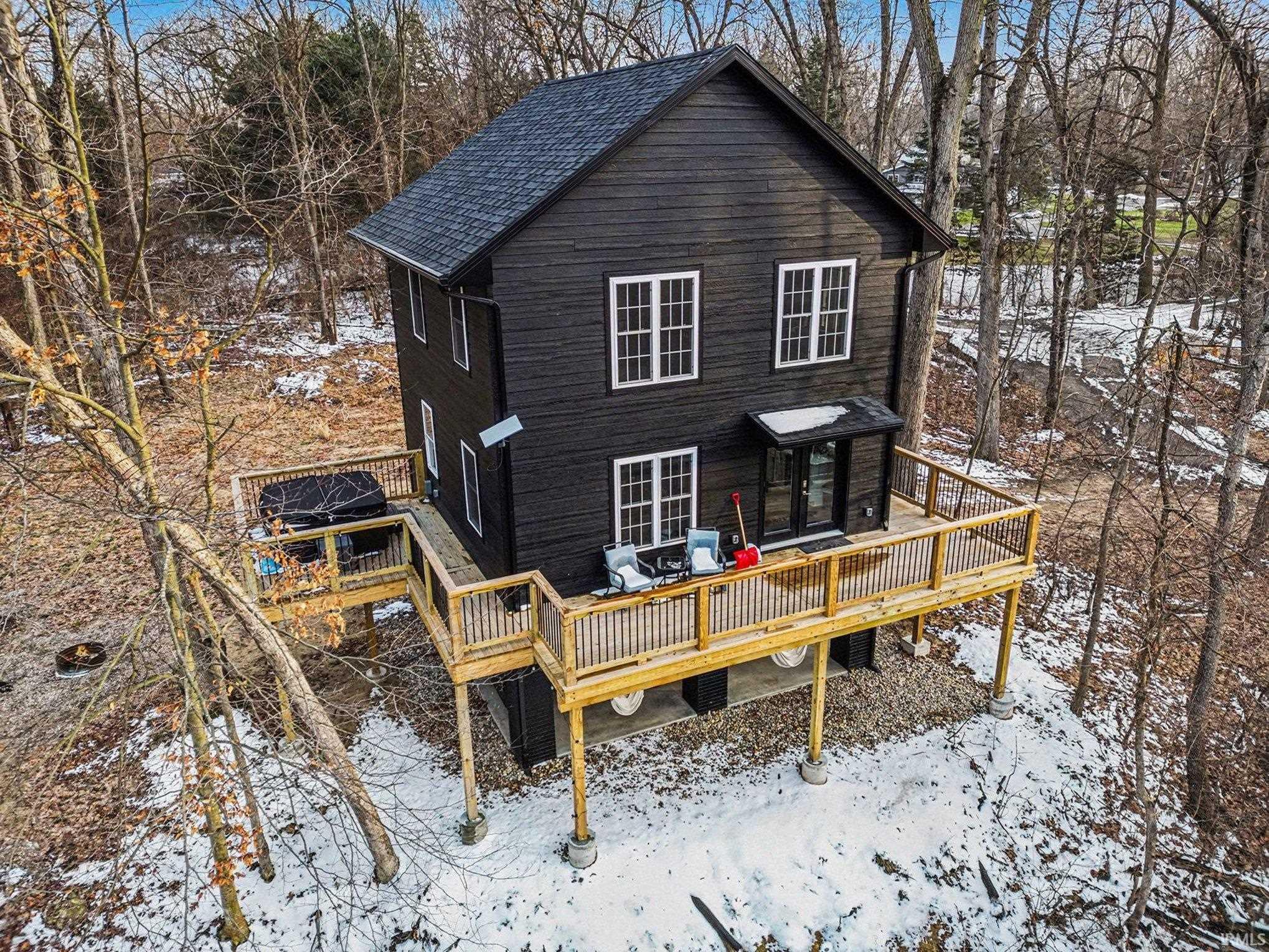 Snow covered rear of property featuring a deck and view of scattered trees