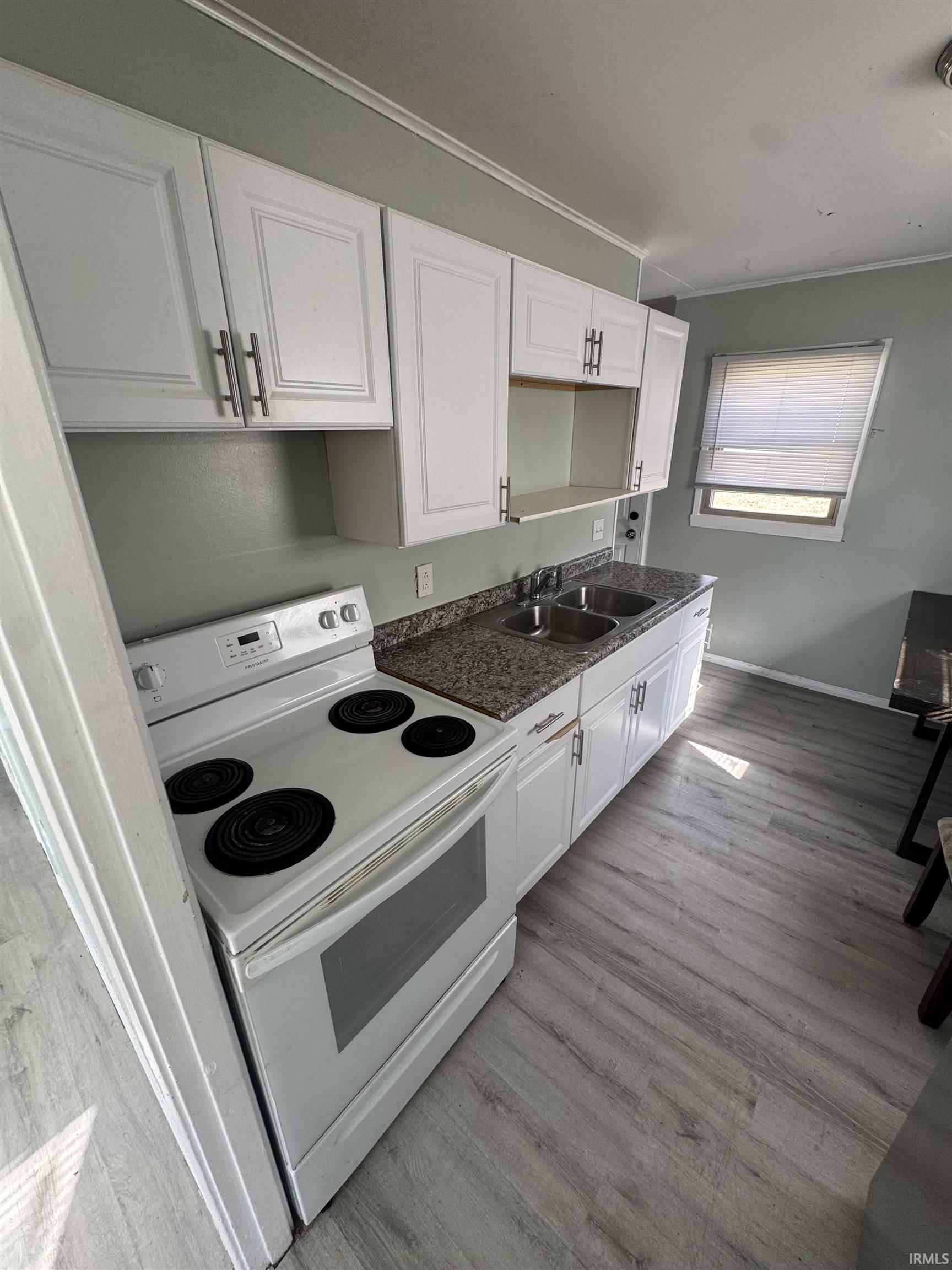 Kitchen featuring electric range, white cabinets, ornamental molding, and light wood-style floors