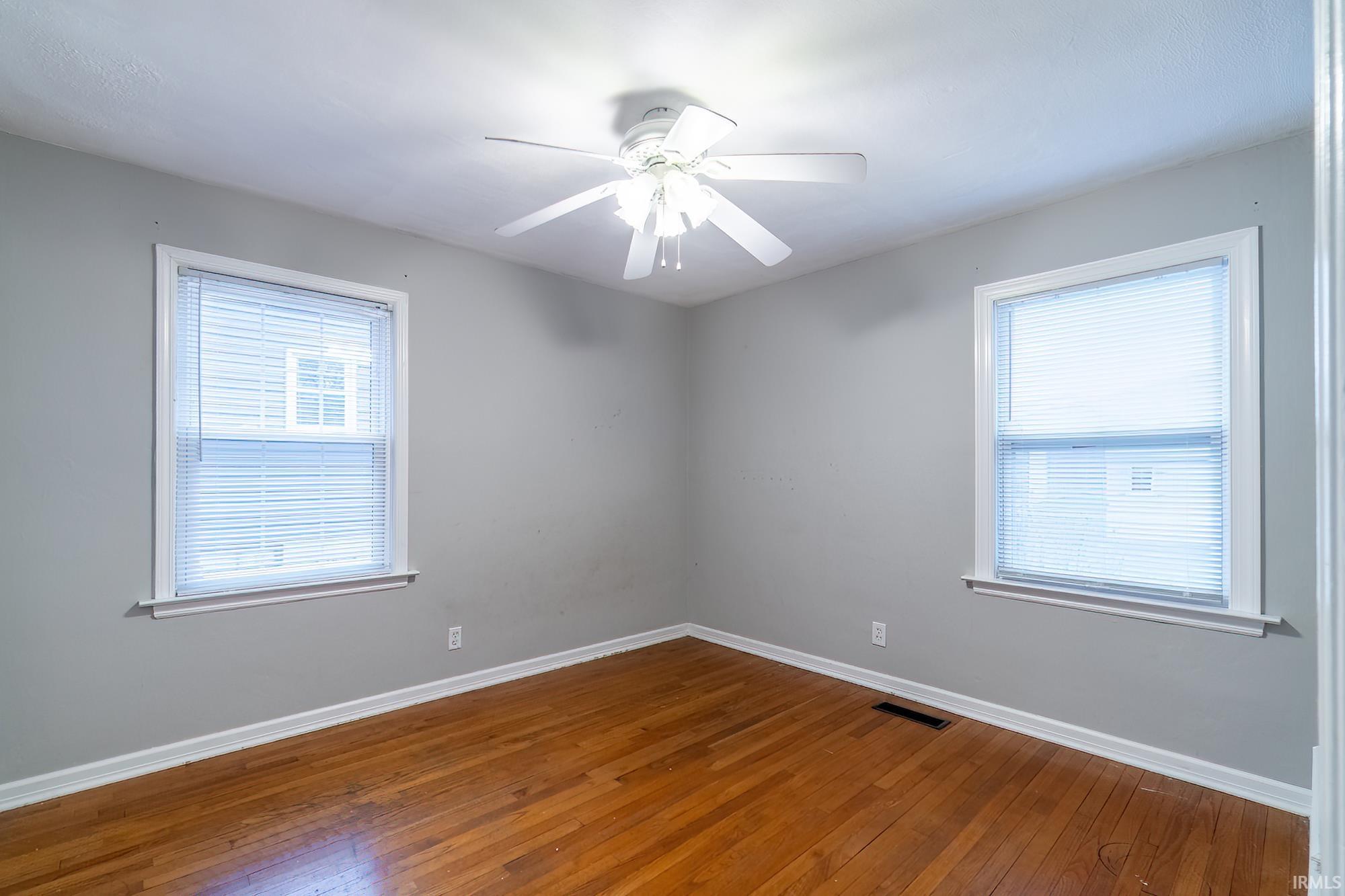 Unfurnished room with dark wood-style floors, a ceiling fan, and healthy amount of natural light