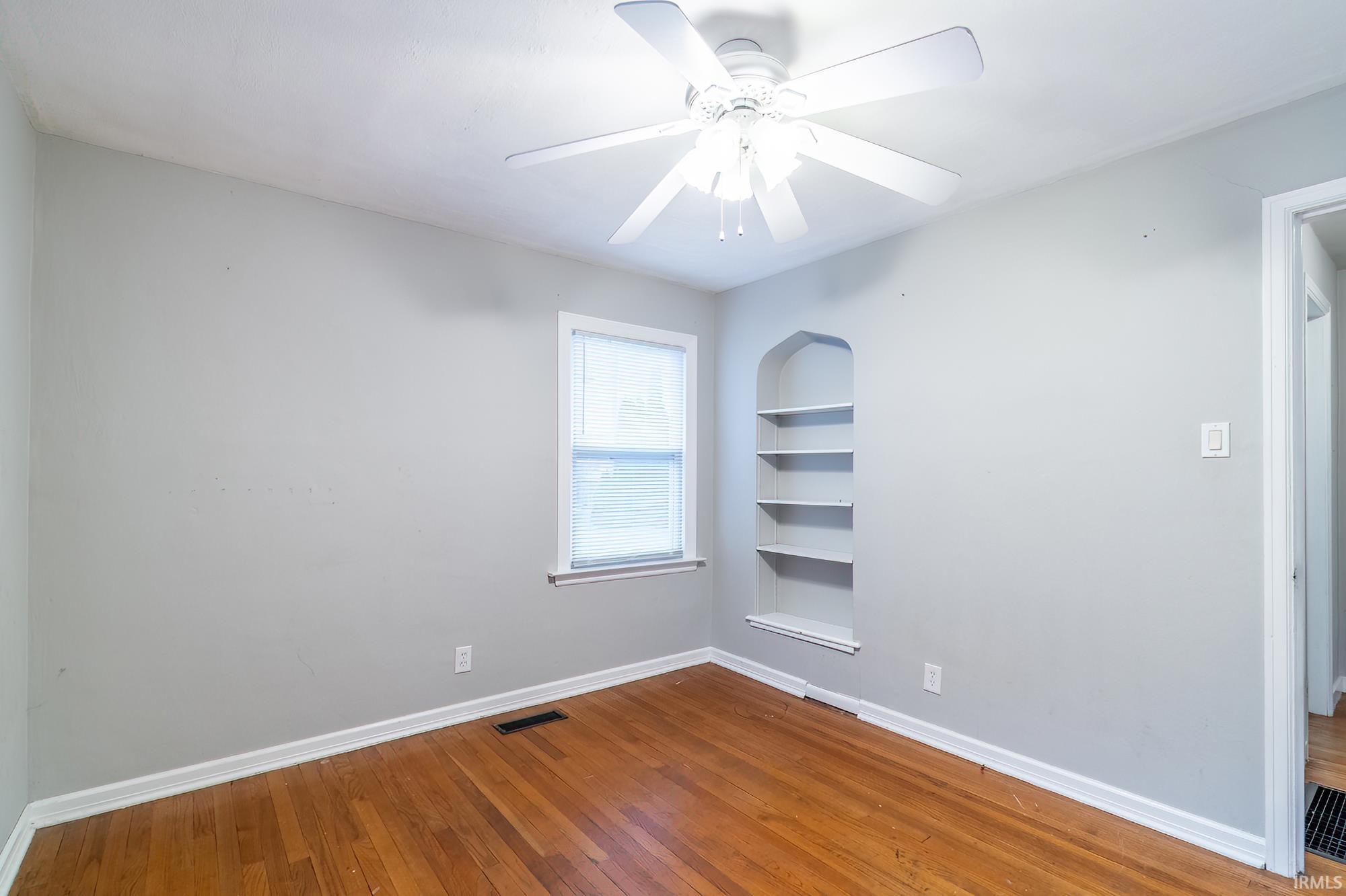 Spare room featuring built in shelves, hardwood / wood-style flooring, and ceiling fan