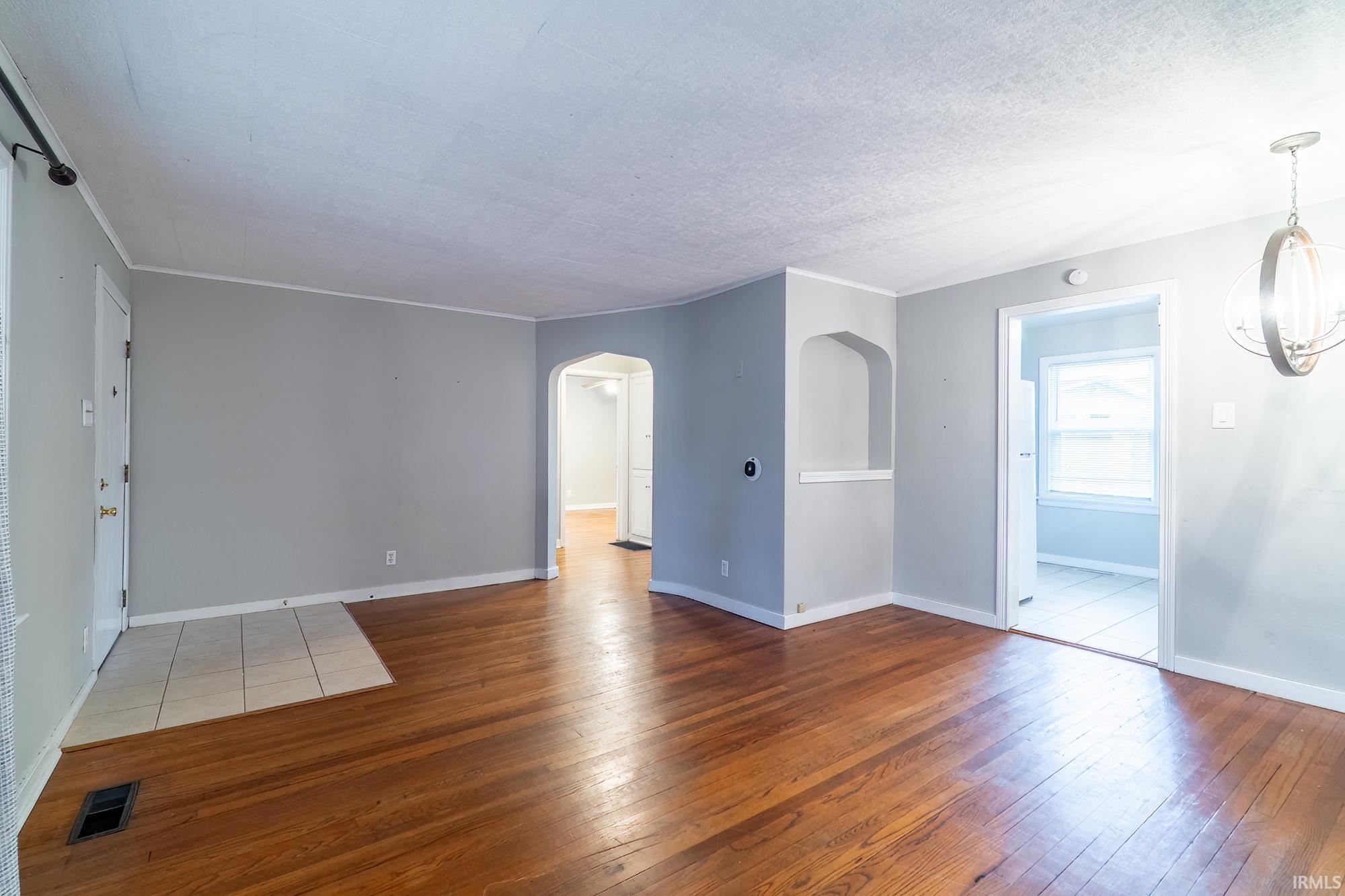 Empty room featuring arched walkways, light wood-style flooring, and a textured ceiling