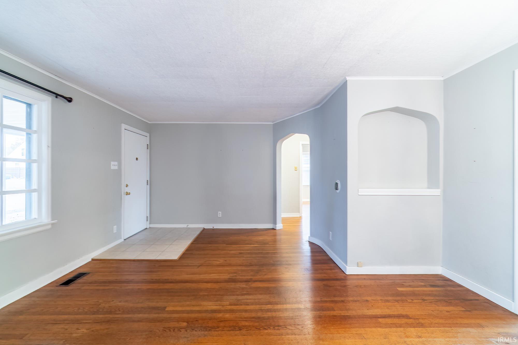 Empty room featuring arched walkways, light wood-type flooring, and crown molding