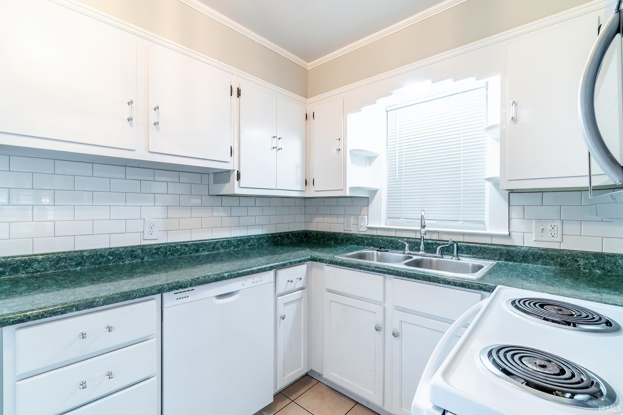 Kitchen with white appliances, dark countertops, white cabinets, light tile patterned floors, and backsplash