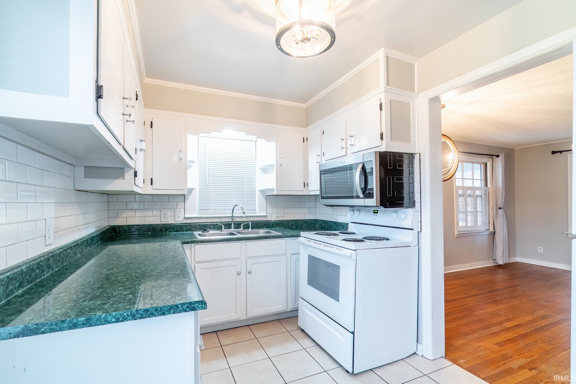Kitchen with white electric range oven, dark countertops, suspended lighting, white cabinetry, and crown molding