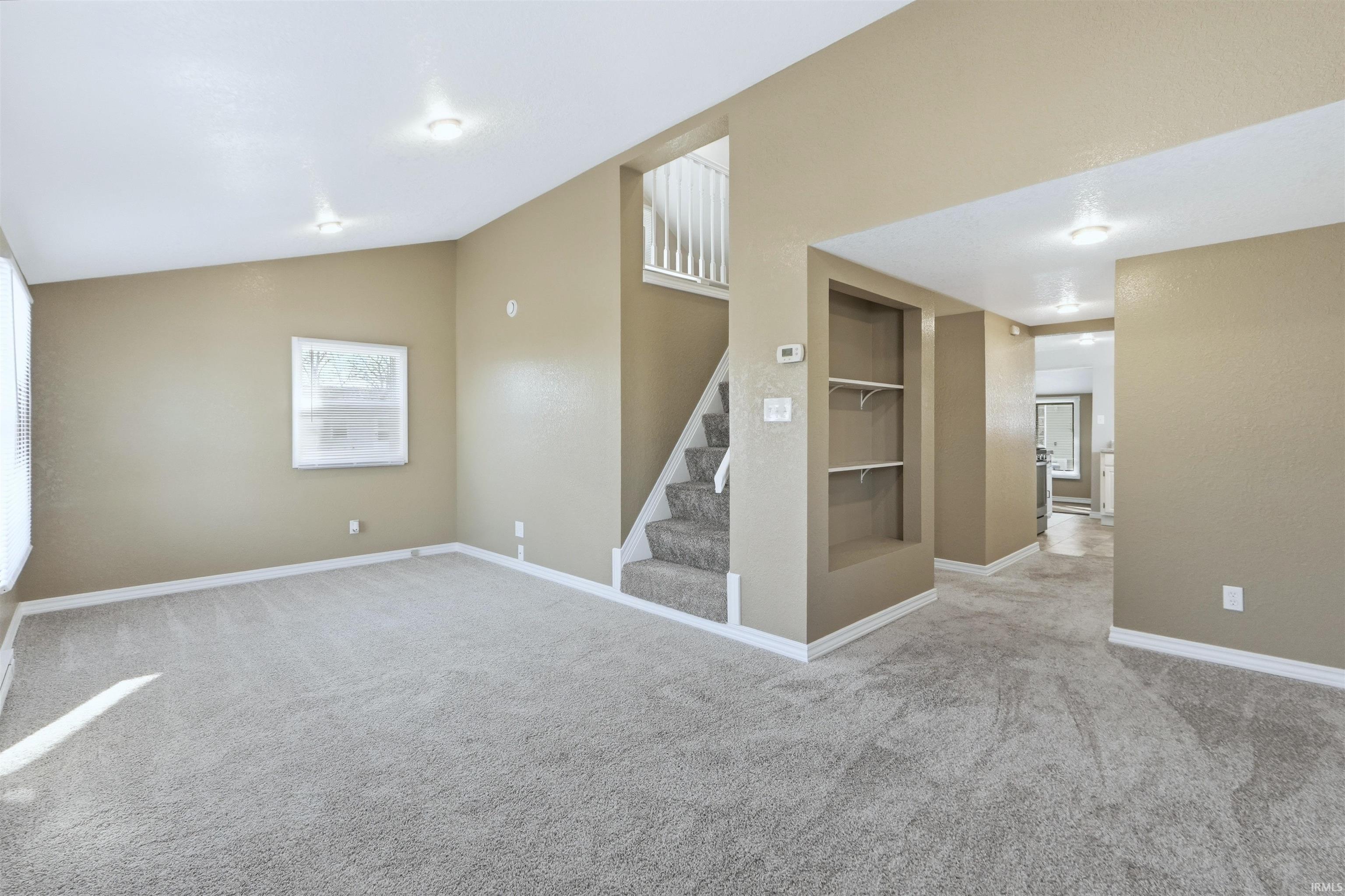 Unfurnished room featuring built in shelves, carpet flooring, and lofted ceiling